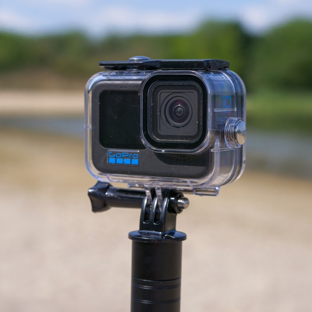 Een GoPro actiecamera in een waterdichtebehuizing op een zwarte selfiestick buiten.