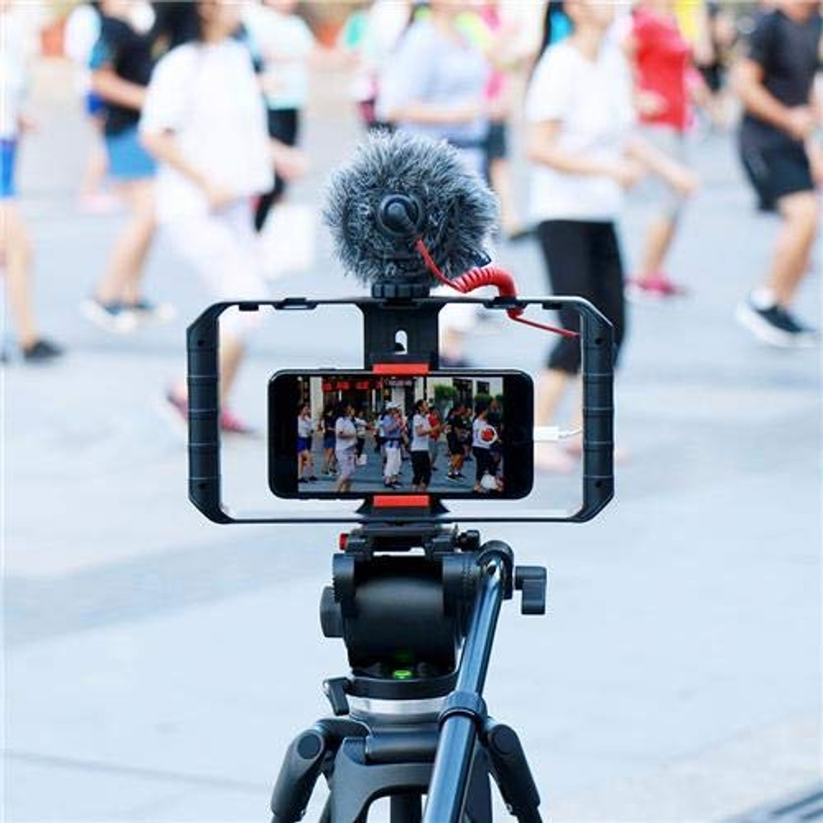 Een smartphone met microfoon op een statief filmt mensen op de achtergrond.
