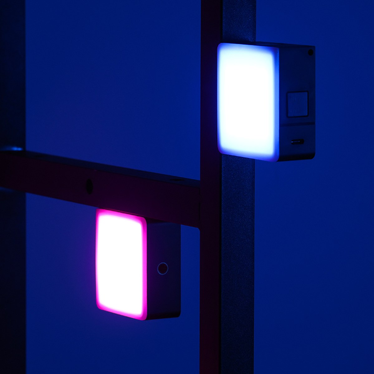 Dos luces LED cuadradas con iluminación azul y rosa están unidas a una estructura metálica oscura.