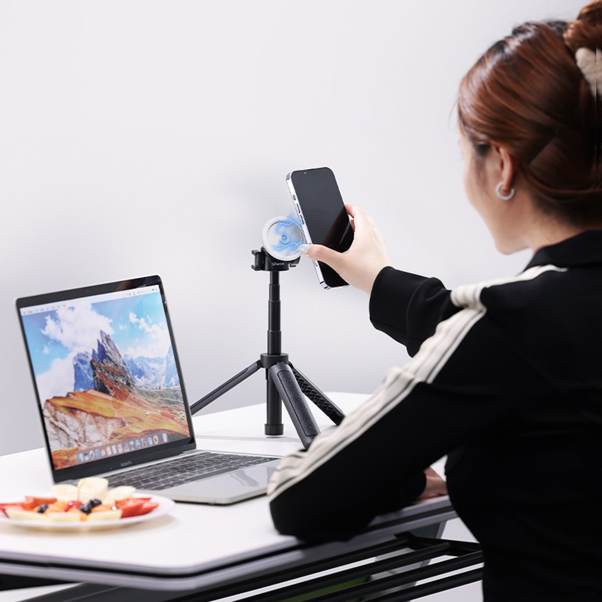 Een vrouw plaatst een smartphone op een magnetische houder op een bureau naast een laptop.