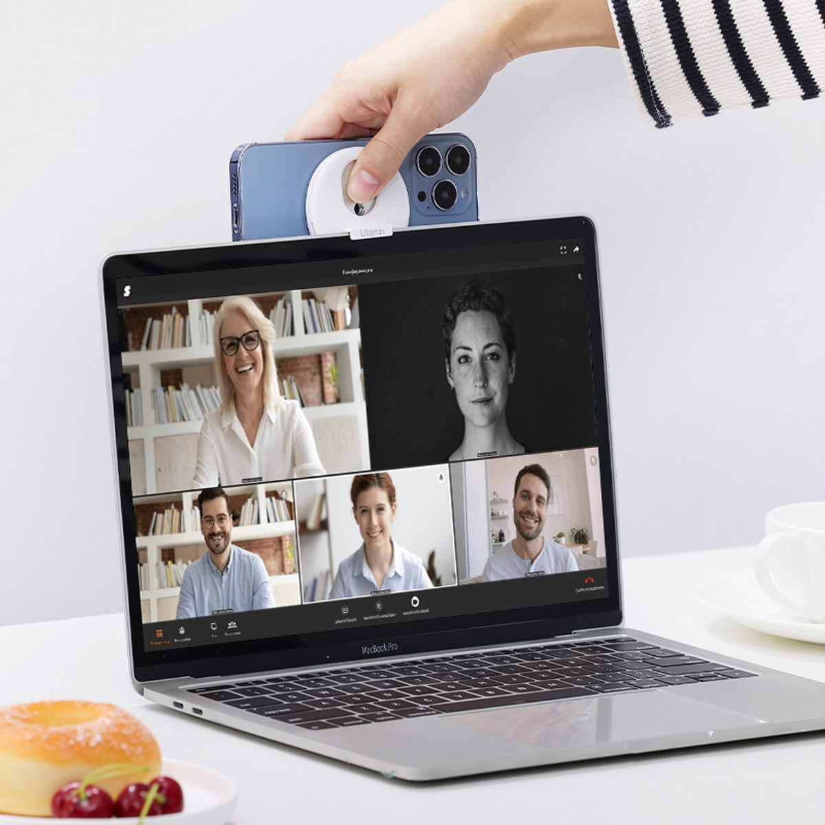 Een hand bevestigt een blauwe smartphone met ringlamp op een laptop die een videobeschrijving toont.
