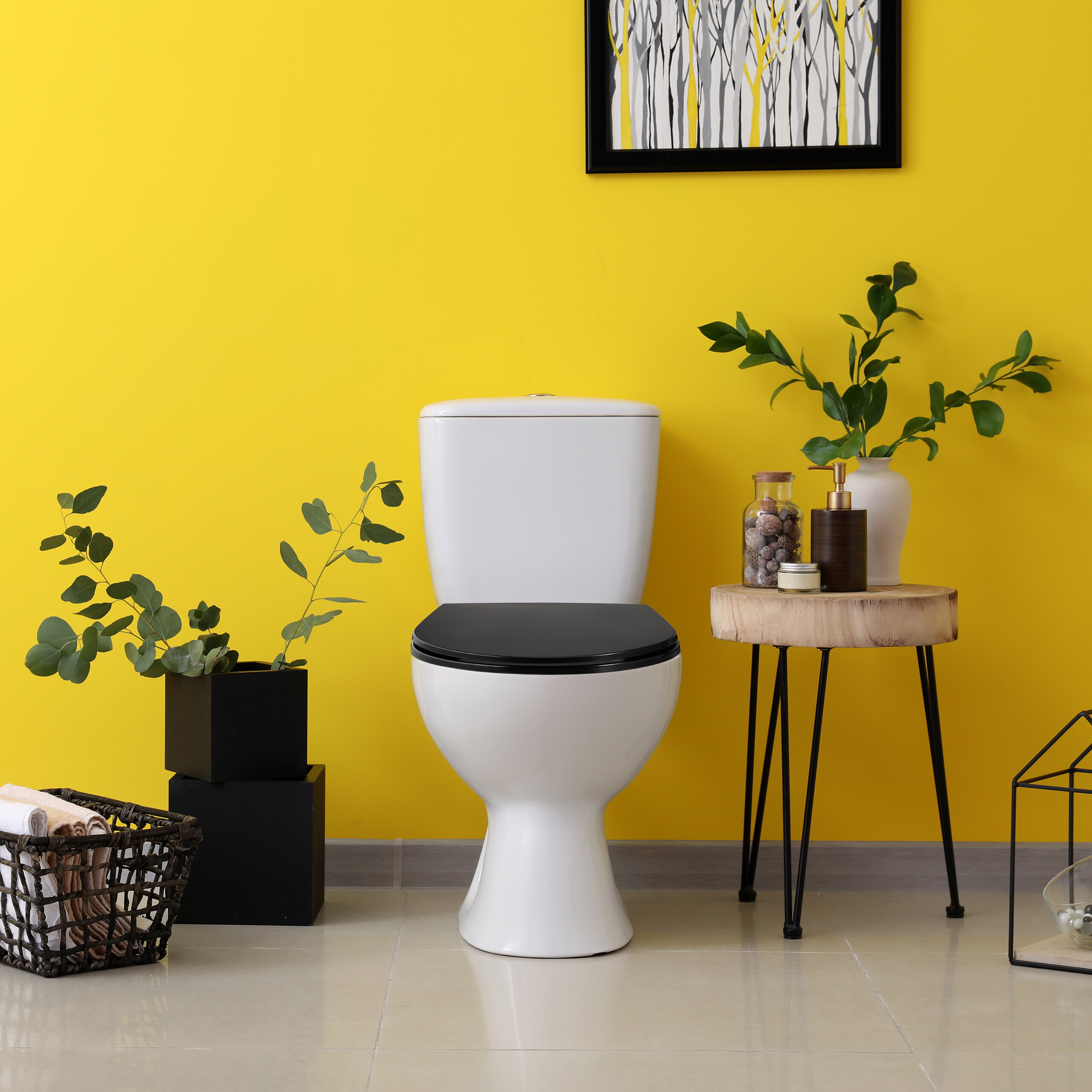 Weißes WC mit schwarzem Sitz vor gelber Wand, flankiert von Pflanzen und Holztisch mit Dekoration.