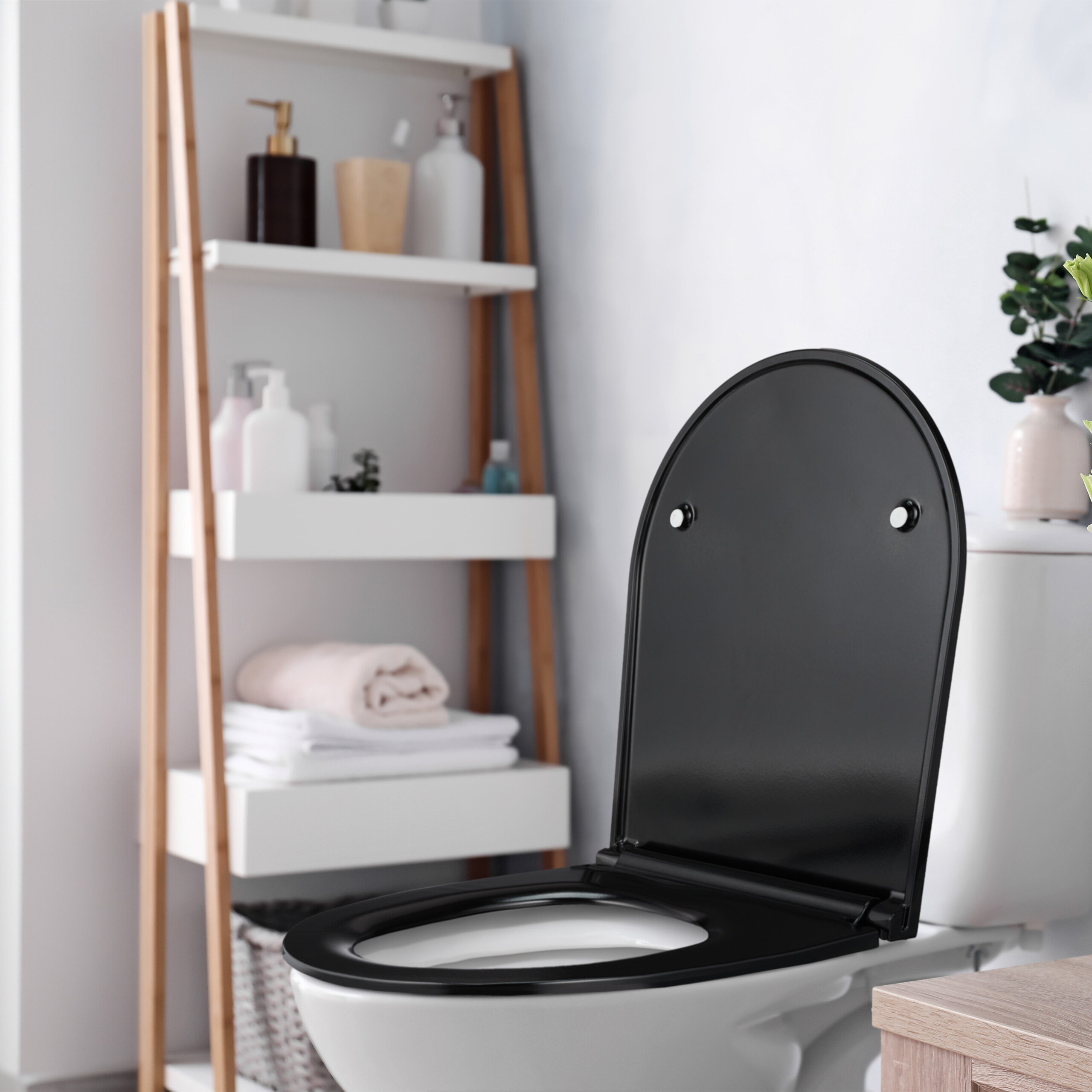 Eine weiße Toilette mit schwarzem Deckel steht in einem Badezimmer, im Hintergrund ein Regal mit Handtüchern.