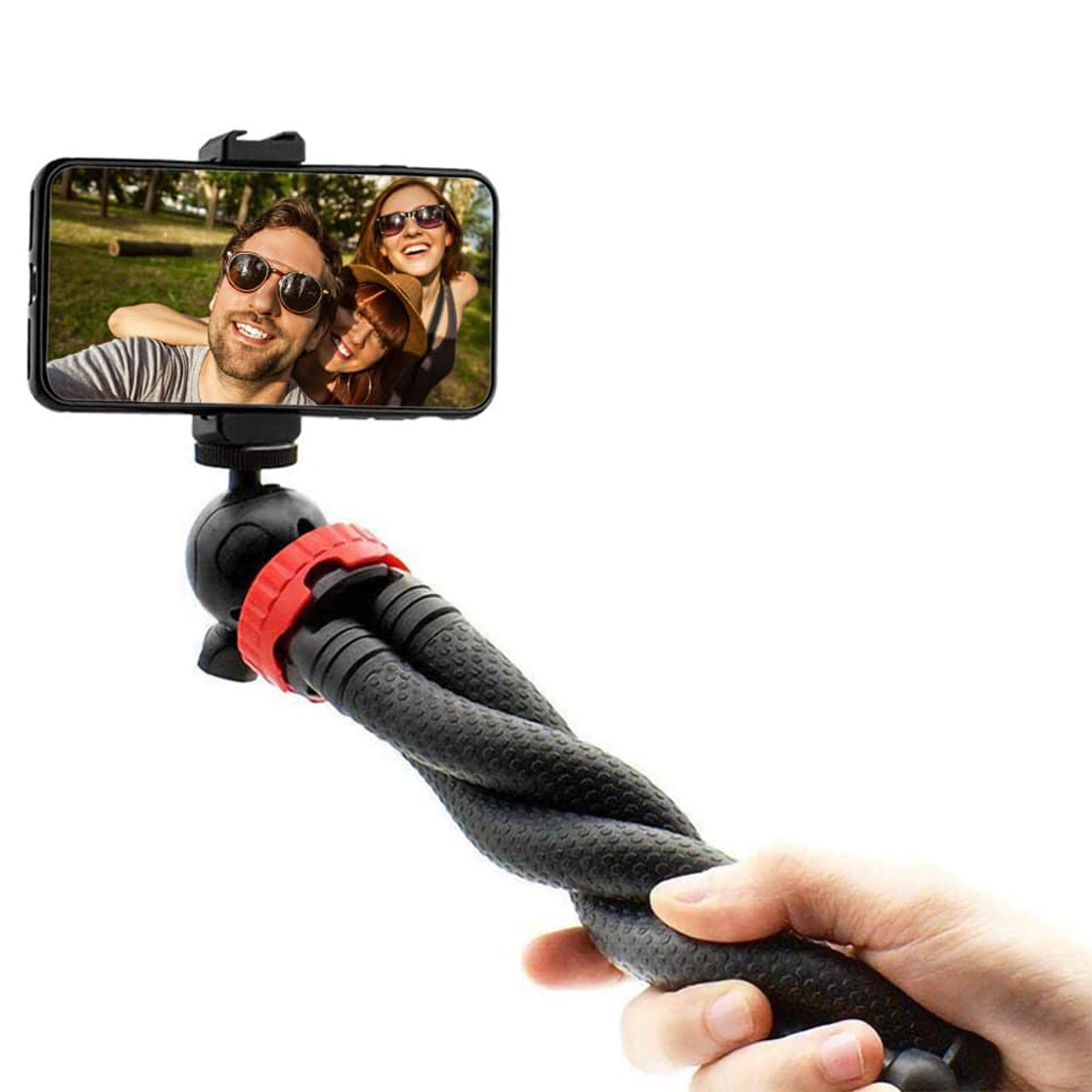 Hand holding a small black flexible tripod. A smartphone mounted on top displays a photo of three smiling people outdoors.