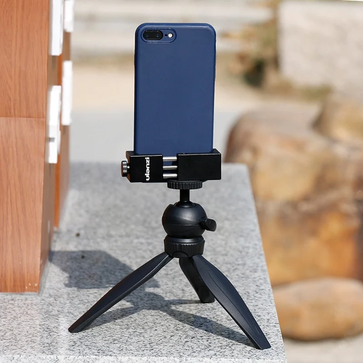 Ein blaues Smartphone in einer Klemme auf einem schwarzen Ministativ auf einer grauen Granitoberfläche.