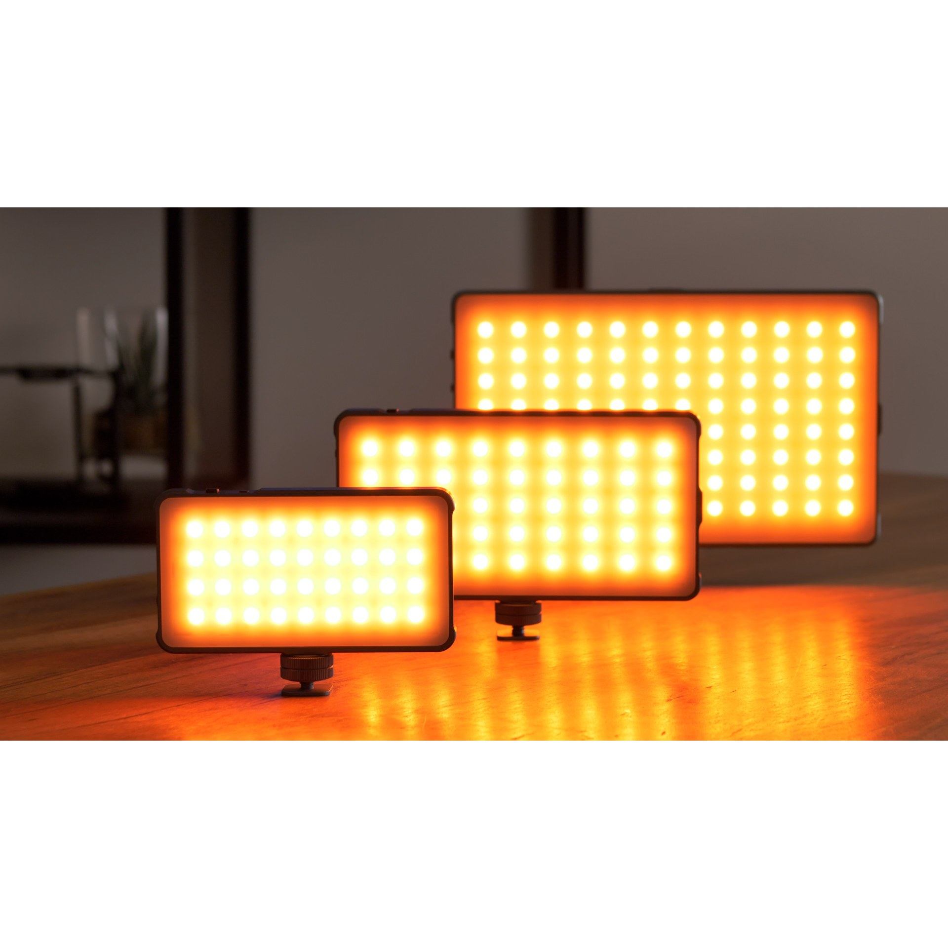 Three illuminated LED panels of different sizes stand on a wooden table.