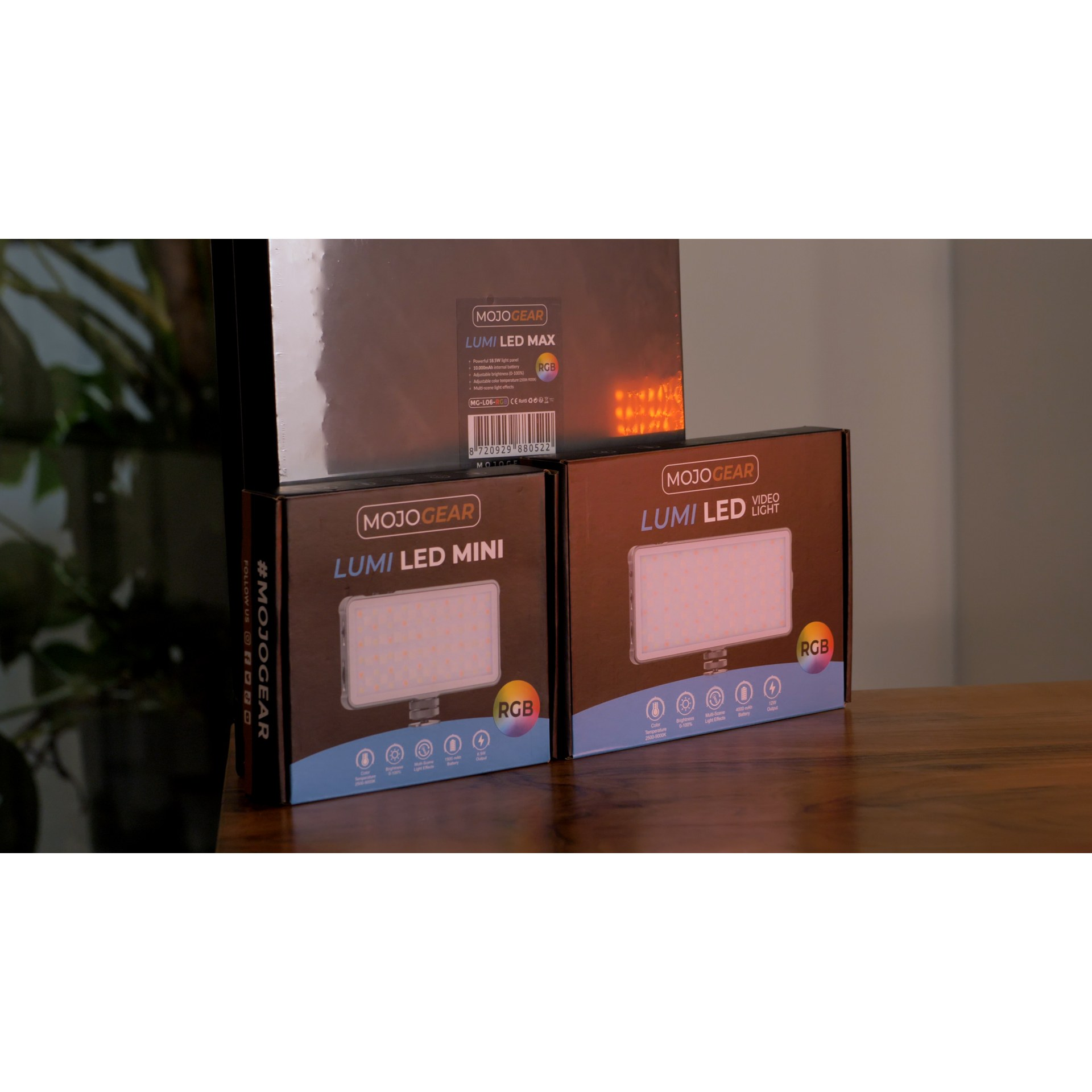 Three MojoGear LED light boxes on a wooden table, featuring Mini, Max, and Video Light variants.