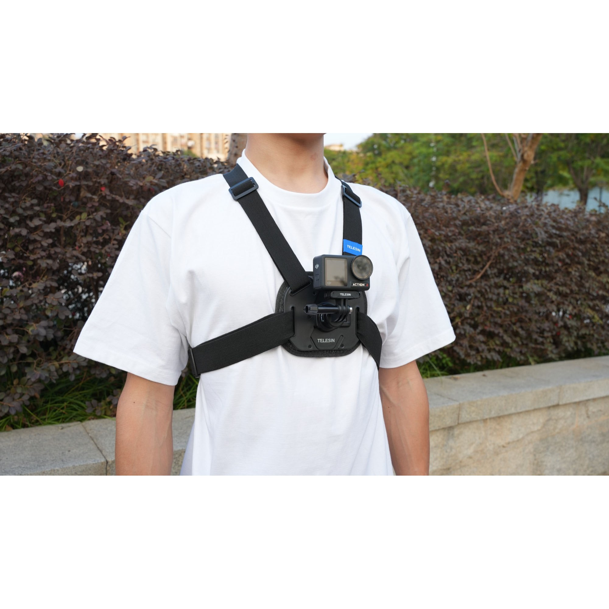 Iemand in een wit t-shirt draagt een actioncam op een borsttuig voor een heg.