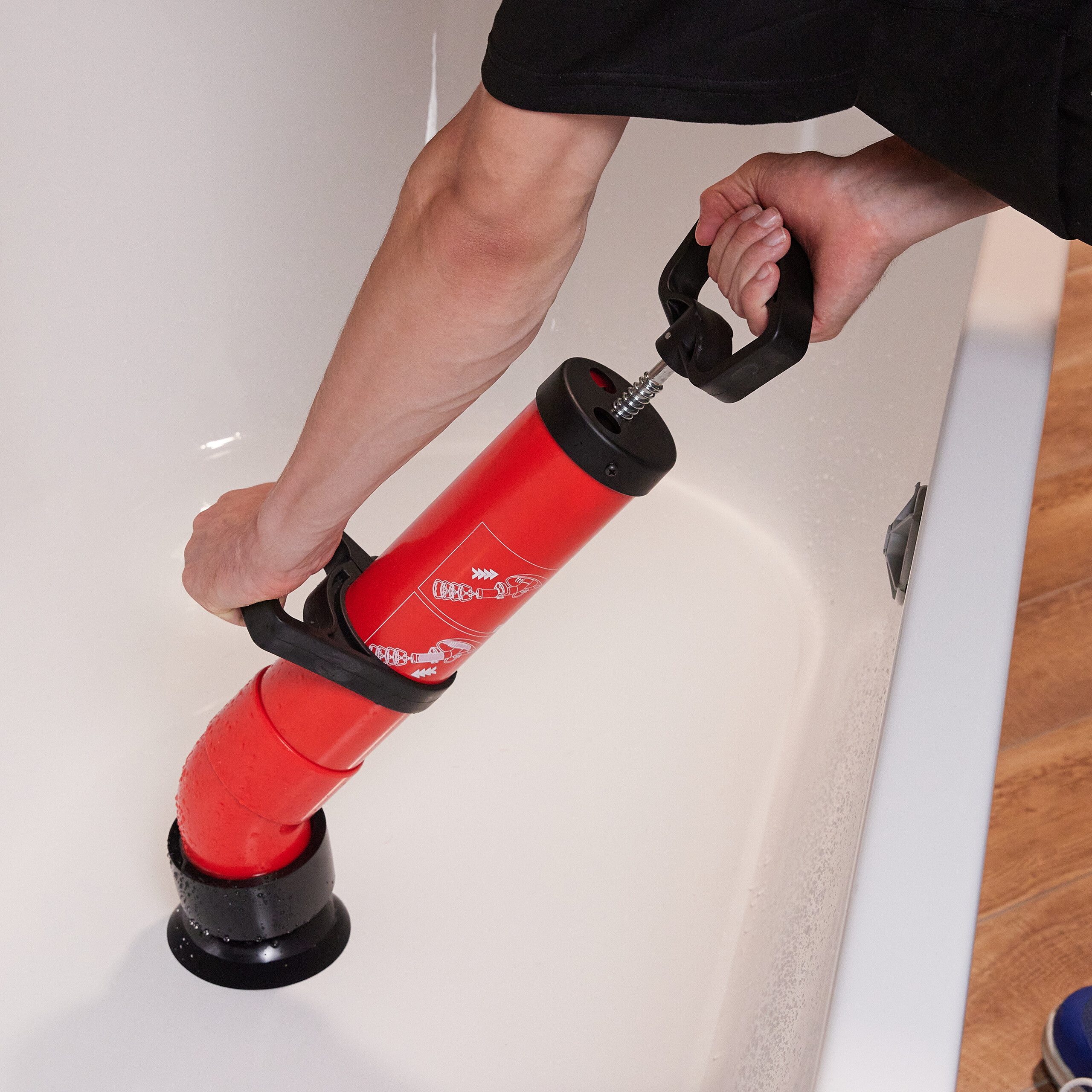 Eine Person benutzt eine rote und schwarze Handabflusspumpe in einer weißen Badewanne.