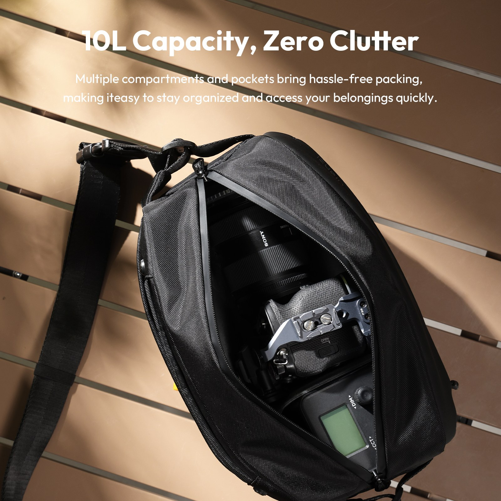 A black camera sling bag filled with a camera and accessories rests on a wooden slat table.