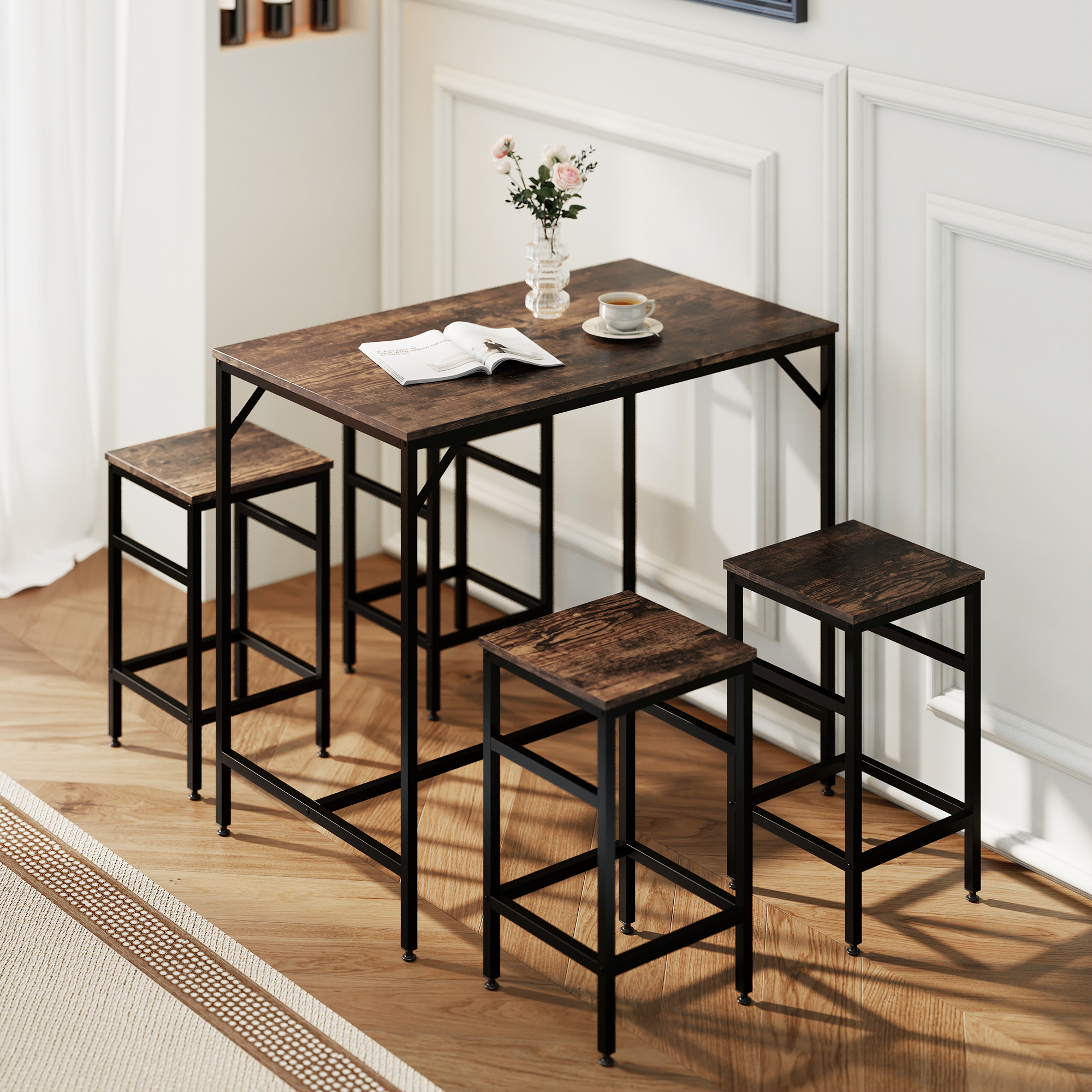 Un tavolo in legno con struttura in metallo nero, quattro sgabelli, una tazza, fiori e un libro aperto.