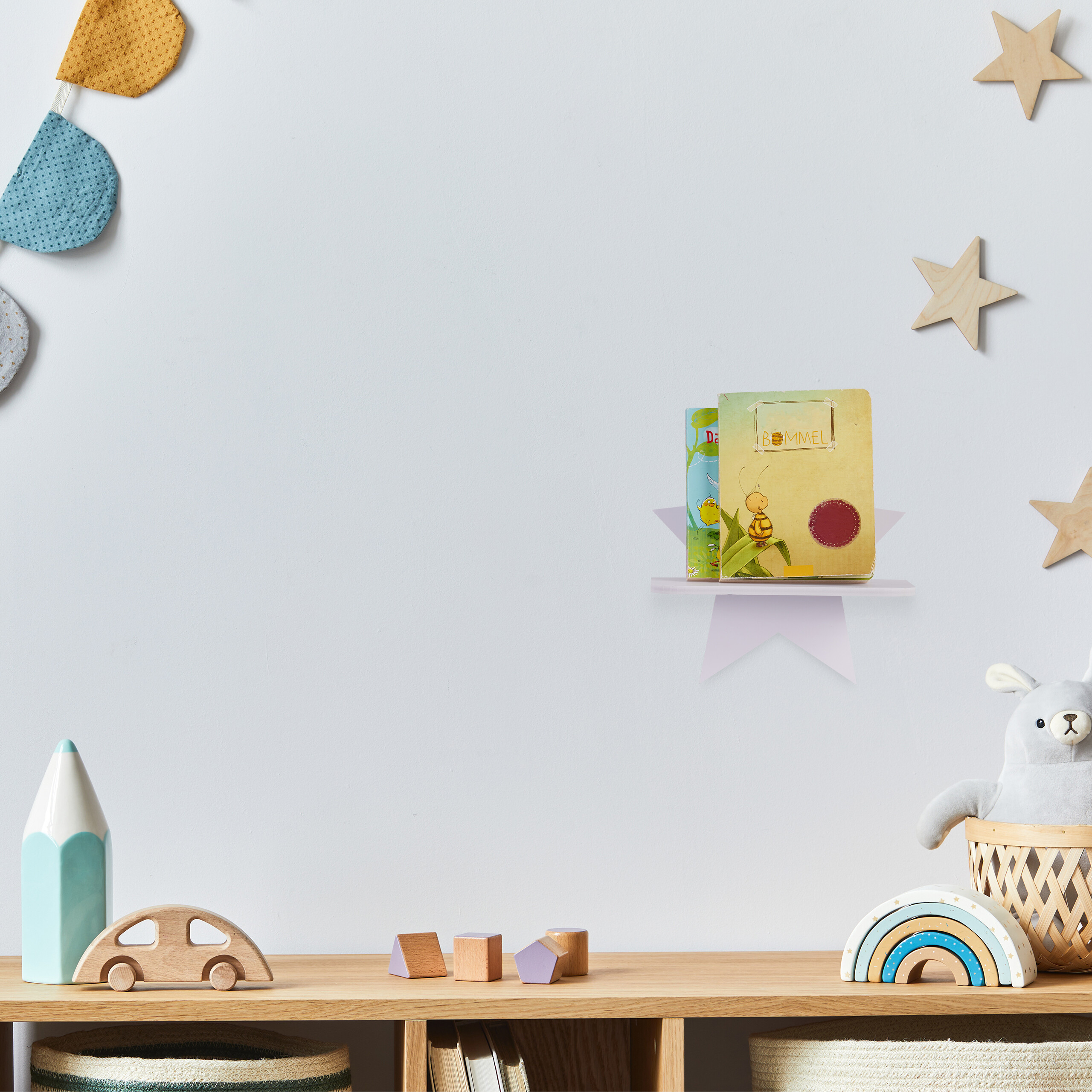 Ein Kinderzimmer mit einem Holztisch mit Spielzeug, einem kleinen Wandregal und Sternendekorationen.