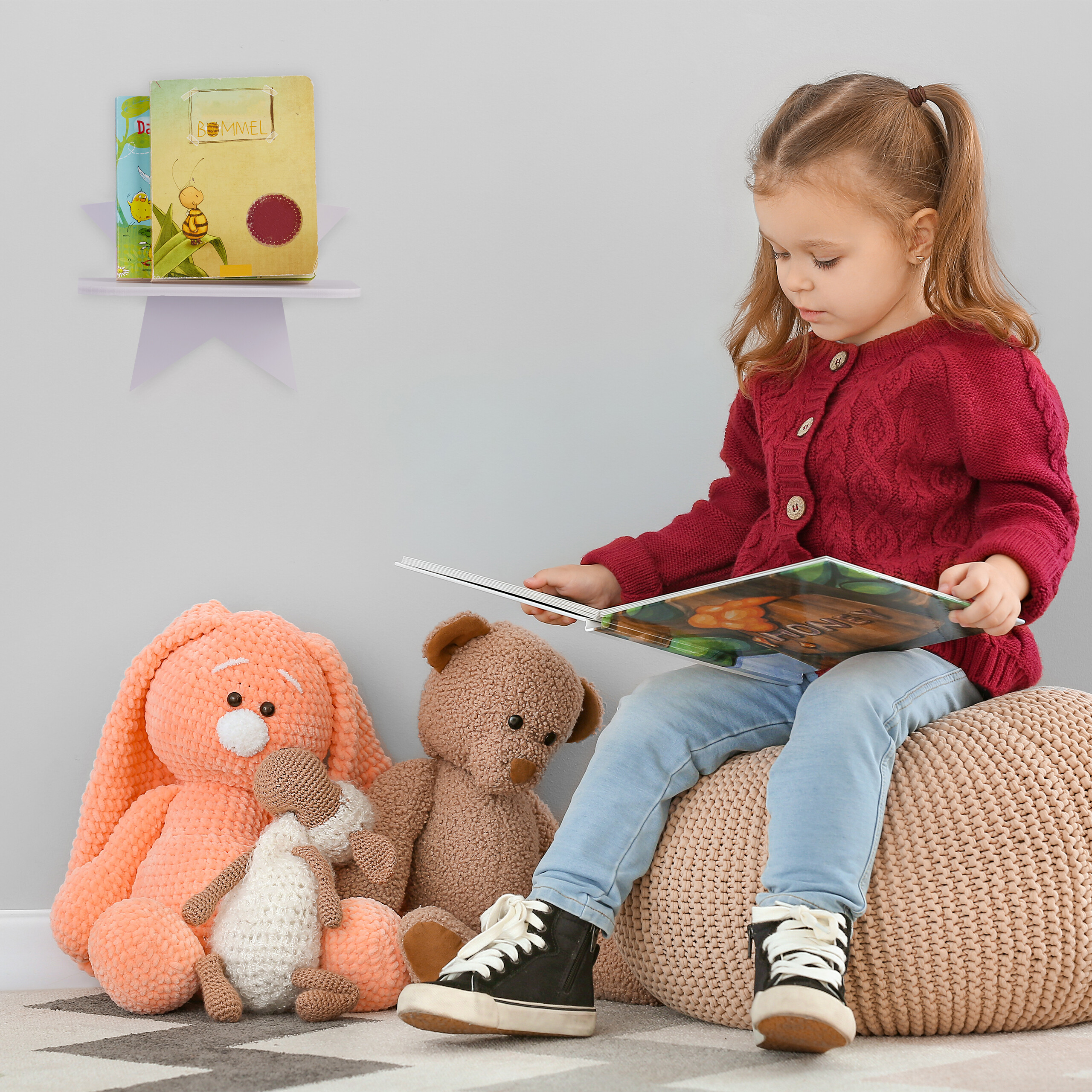 Ein junges Mädchen in rotem Pullover sitzt auf einem Pouf und liest ein Buch, umgeben von Plüschtieren.