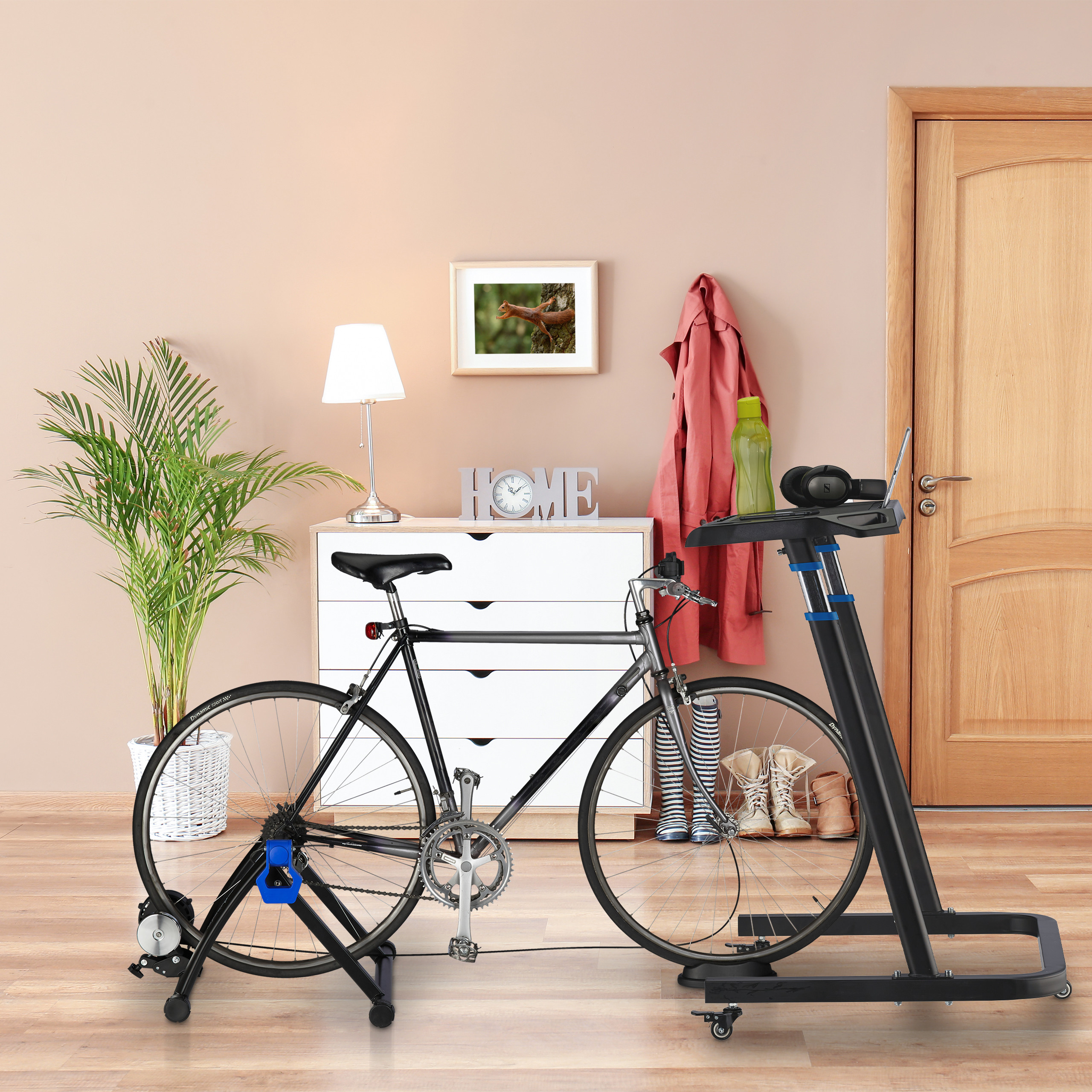 Heimtrainer-Fahrrad auf einem Ständer vor einer Kommode, einer Pflanze, einer Lampe und einer Holztür.