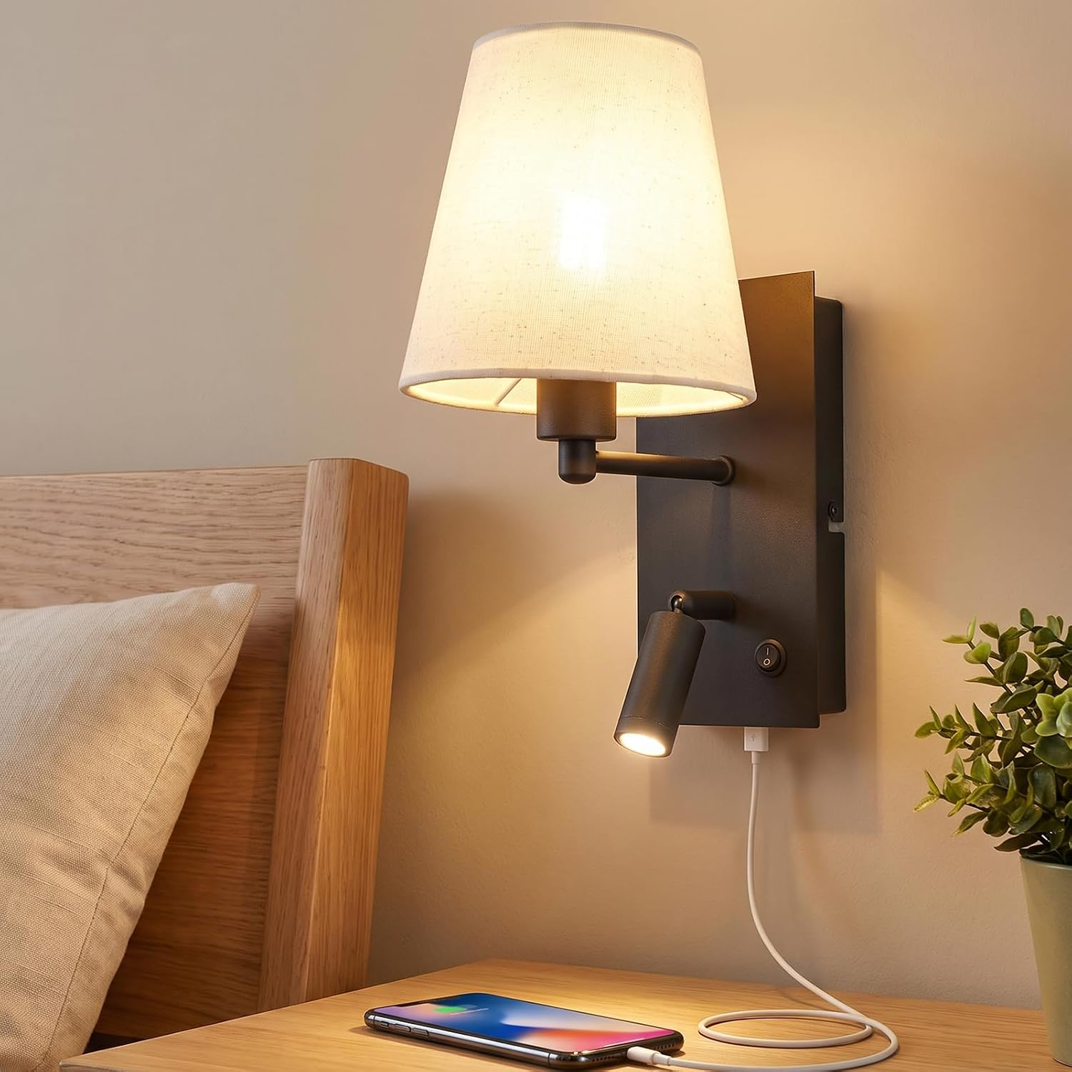 Lampa ścienna z białym kloszem i lampką do czytania nad szafką nocną z telefonem.