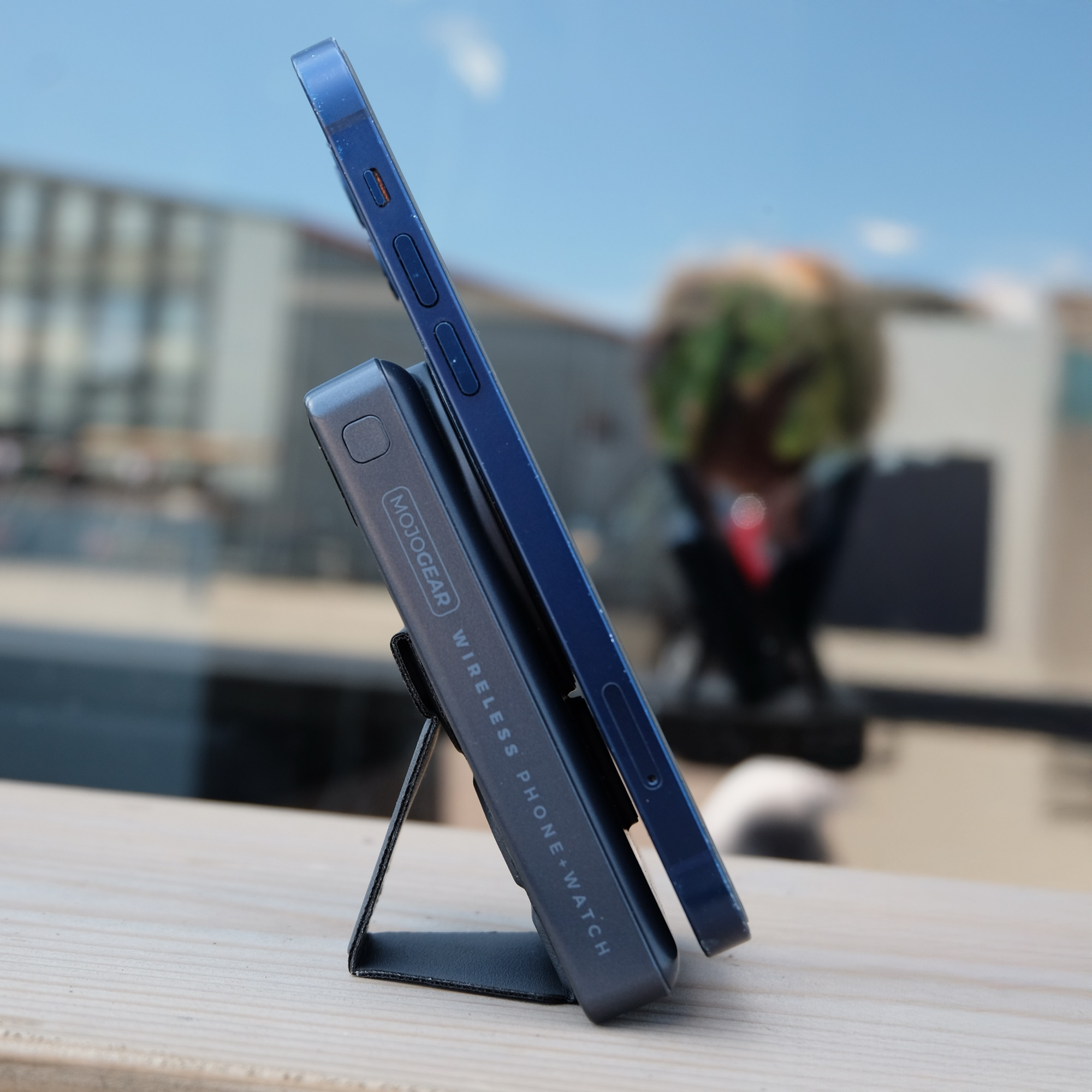 A blue smartphone on a grey MojoGear power bank with a built-in stand, resting on a wooden surface.