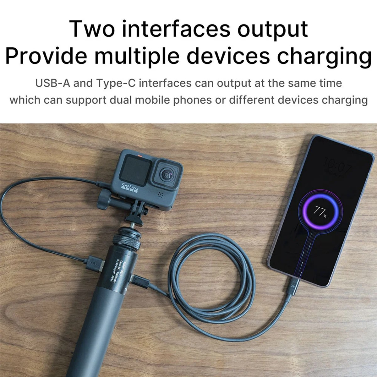 A power bank charges a GoPro camera and a smartphone simultaneously on a wooden table.