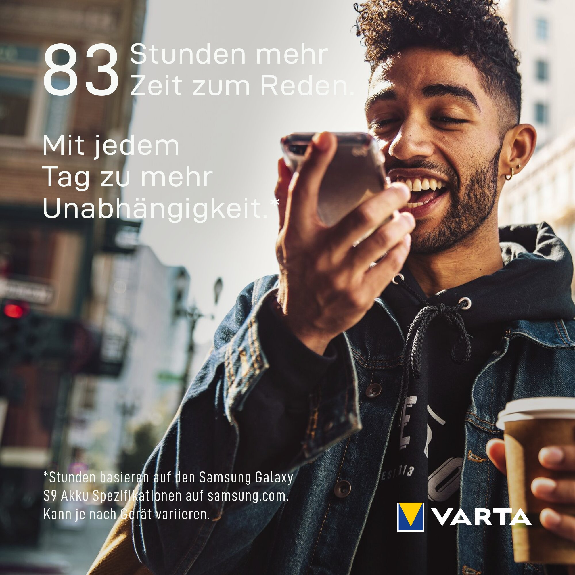 Junger Mann lächelt, während er in einer Stadtlandschaft telefoniert und einen Kaffee hält.
