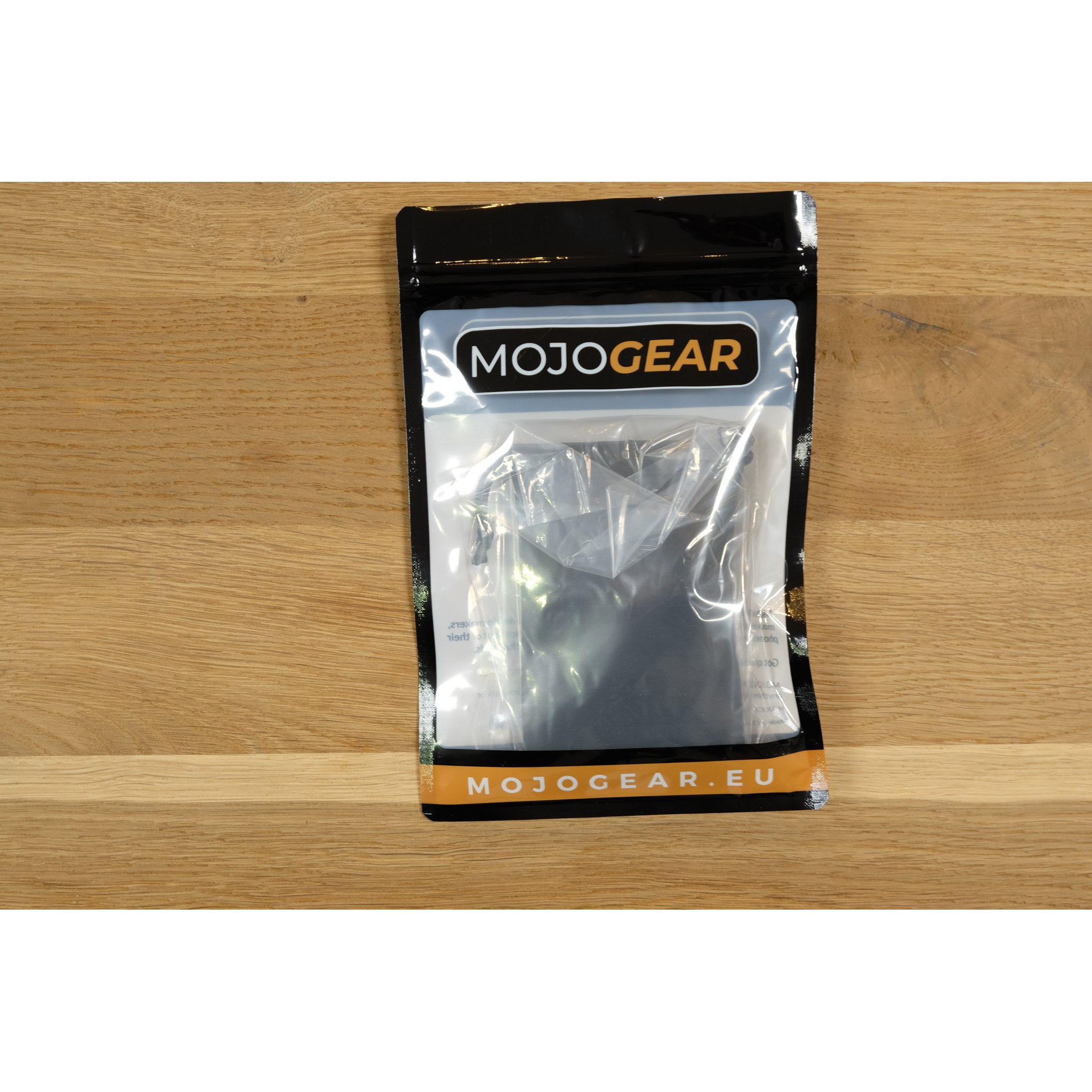 A sealed MojoGear product package resting on a light wooden surface.