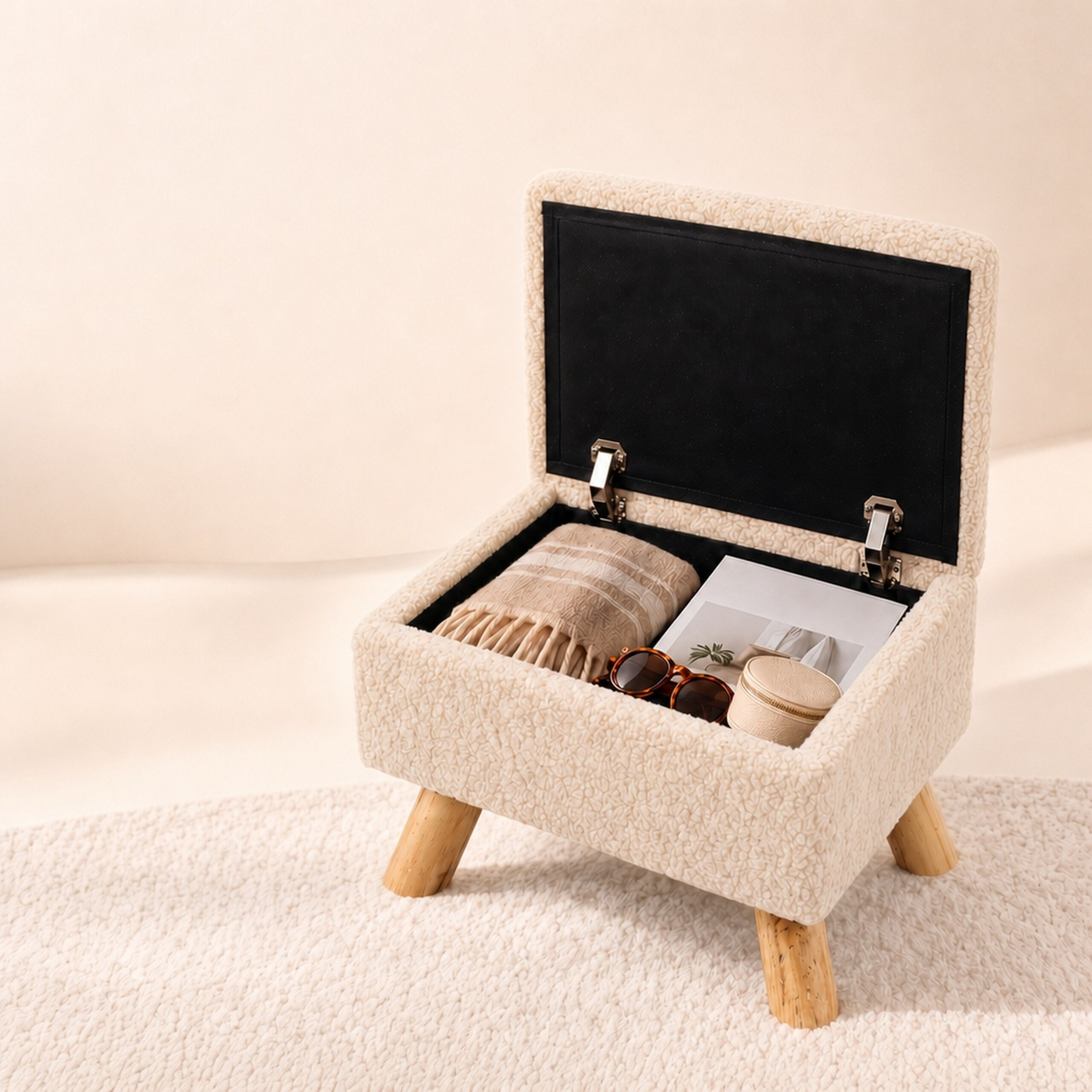 Beiger Fellhocker mit Holzbeinen auf weißem Teppich, Deckel offen, enthält Decke und Sonnenbrille.