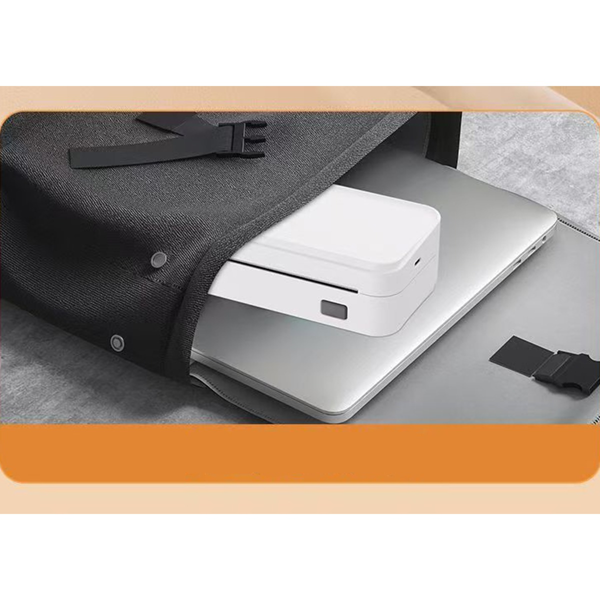 Ein weißes Gerät und ein Laptop in einer offenen schwarzen Tasche auf grauem Untergrund.