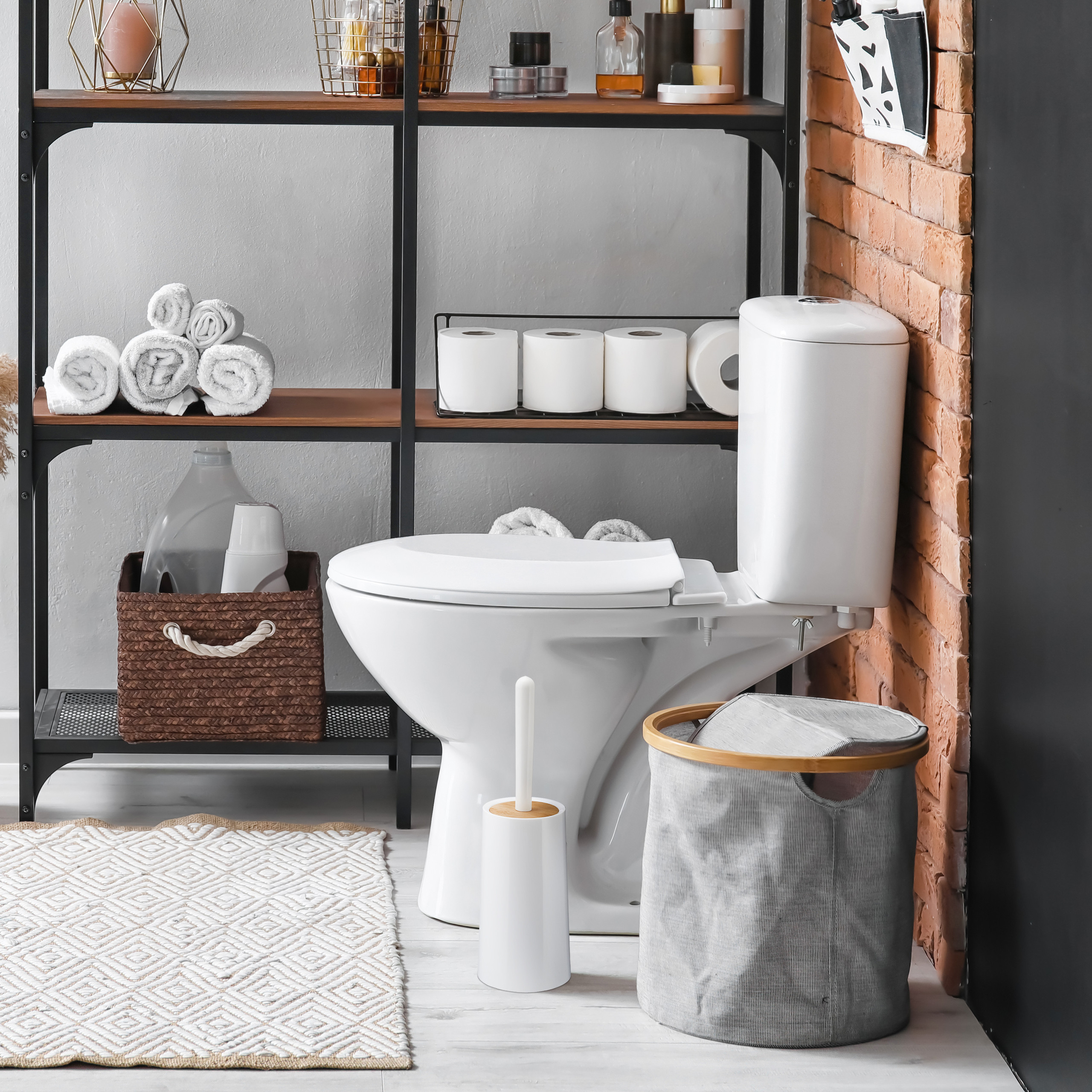 Ein modernes Badezimmer hat eine weiße Toilette, Regale mit Handtüchern, Pflegeprodukten und einen gemusterten Teppich.