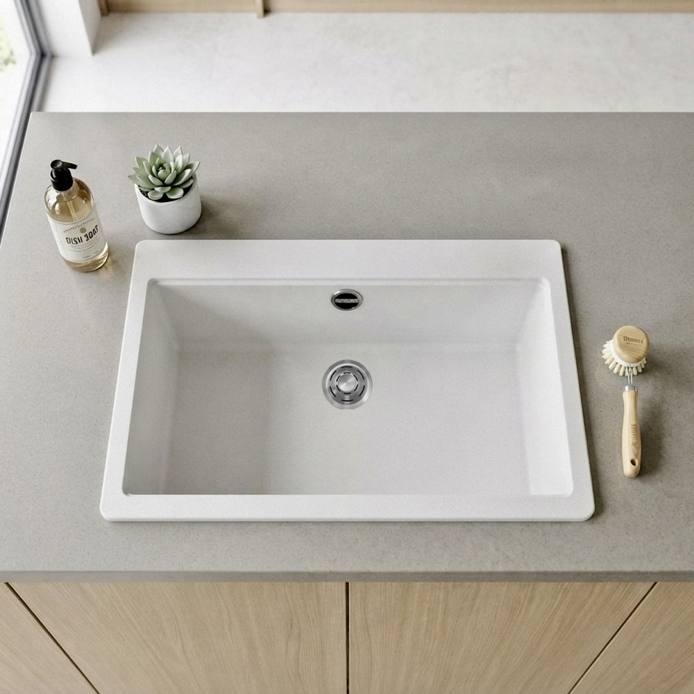 Un lavello bianco su un piano grigio, con sapone, una piantina e una spazzola per piatti.