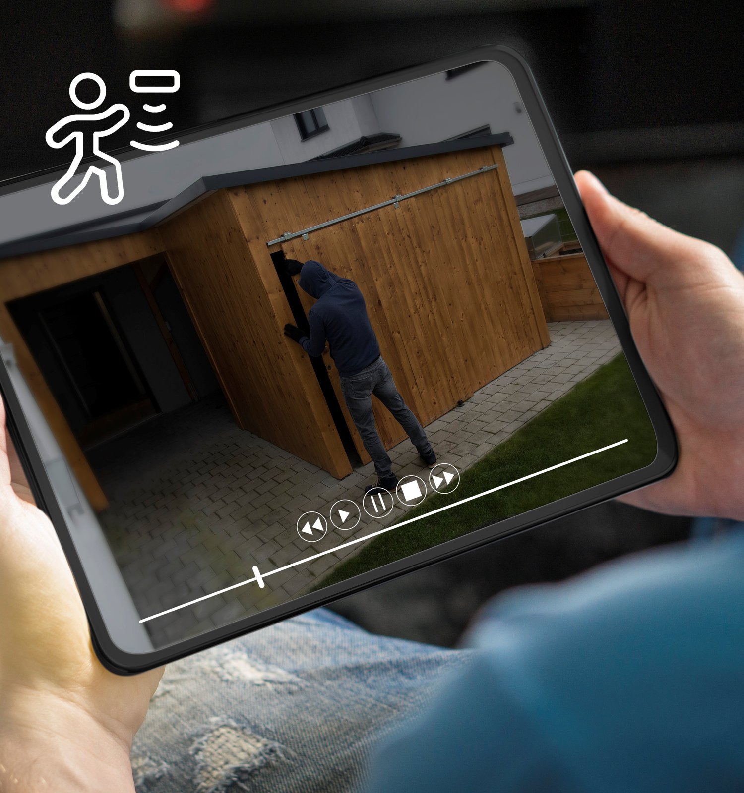 Osoba trzyma tablet z nagraniem przedstawiającym kogoś włamującego się do drewnianej szopy.