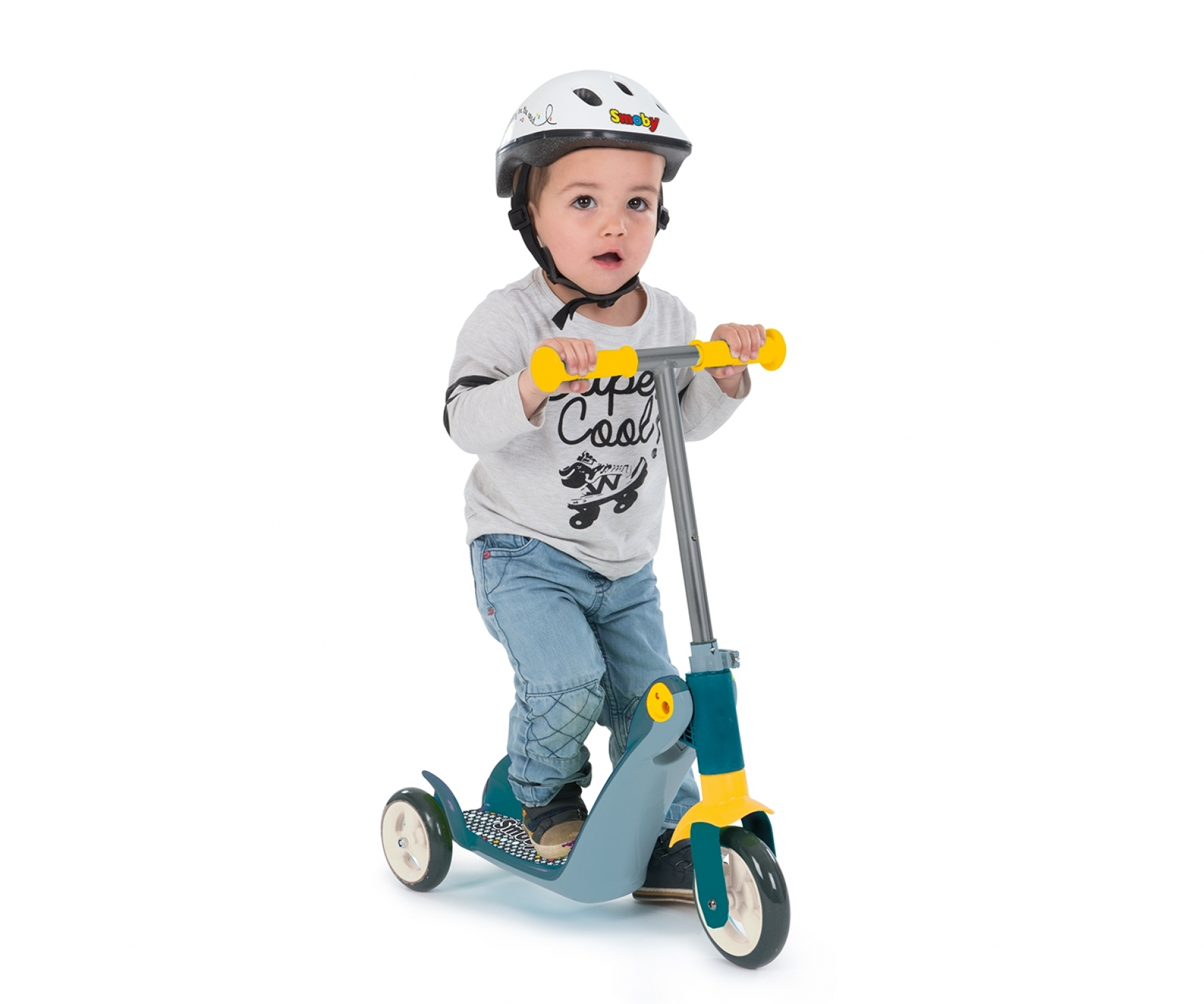 Kleinkind mit Helm fährt auf einem blau-gelben Dreiradroller auf weißem Grund.