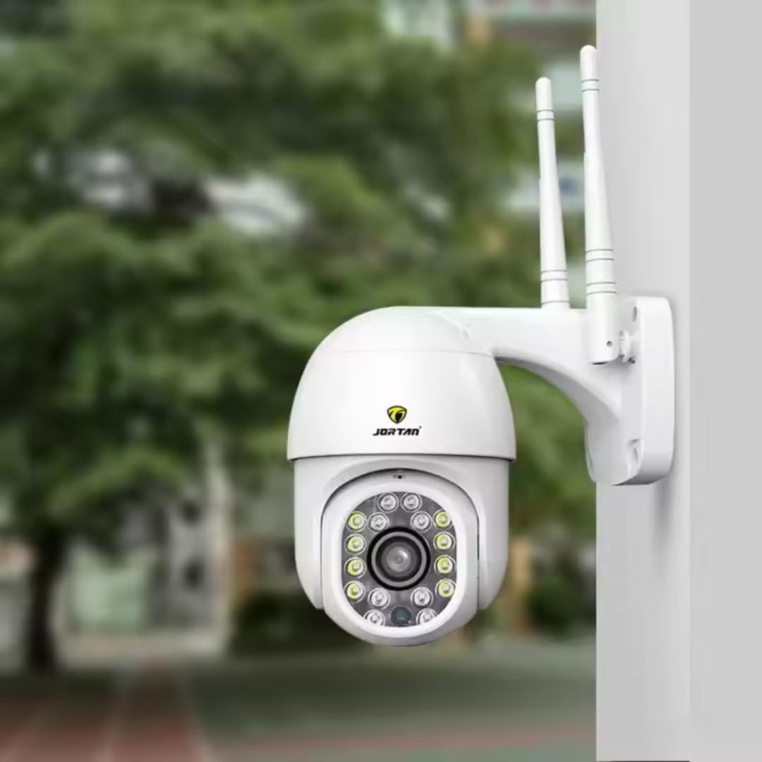 Una cámara de seguridad blanca con dos antenas está montada en la pared frente a un fondo difuso.