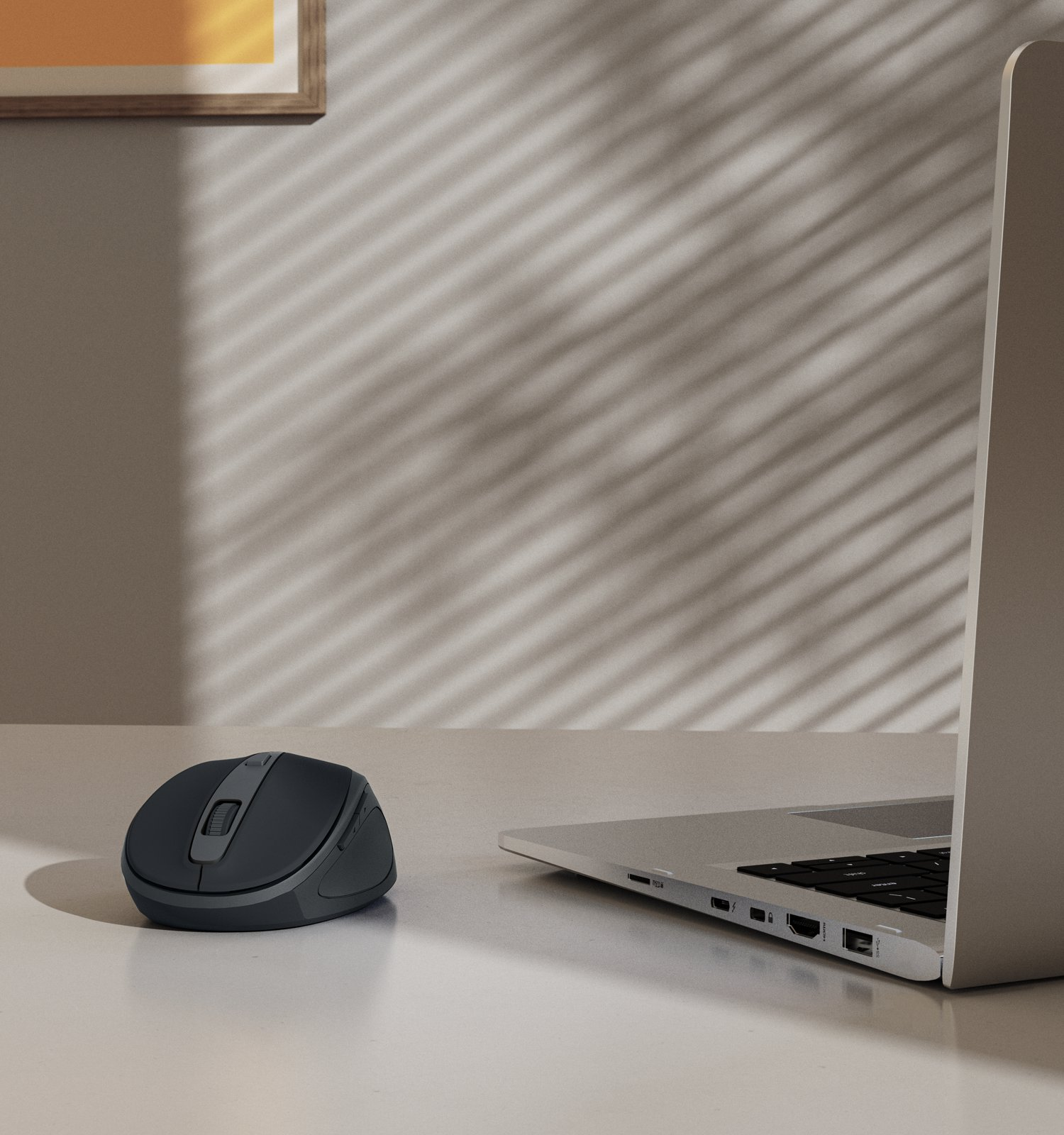 Un mouse per computer grigio e un computer portatile su una scrivania contro una parete con ombre di persiane.