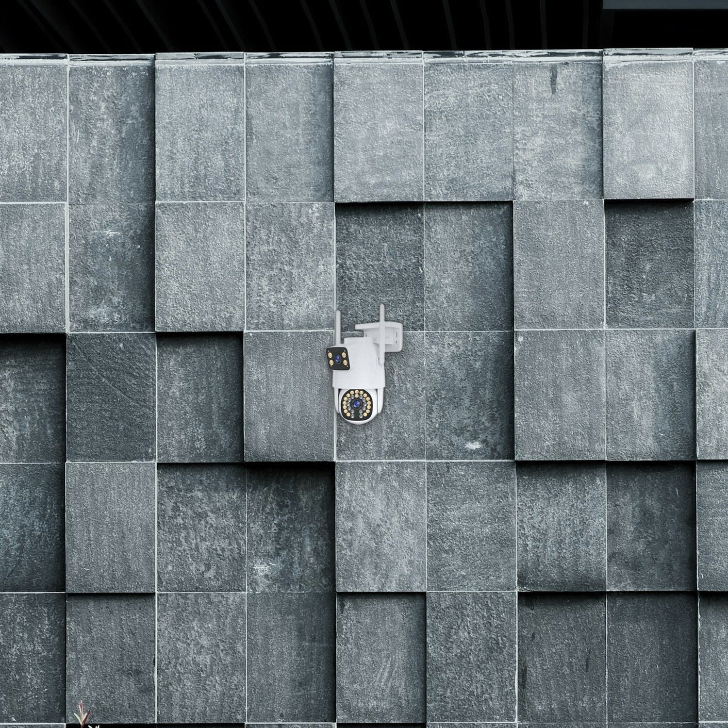 Una cámara de seguridad blanca está montada en una pared de piedra gris texturizada.