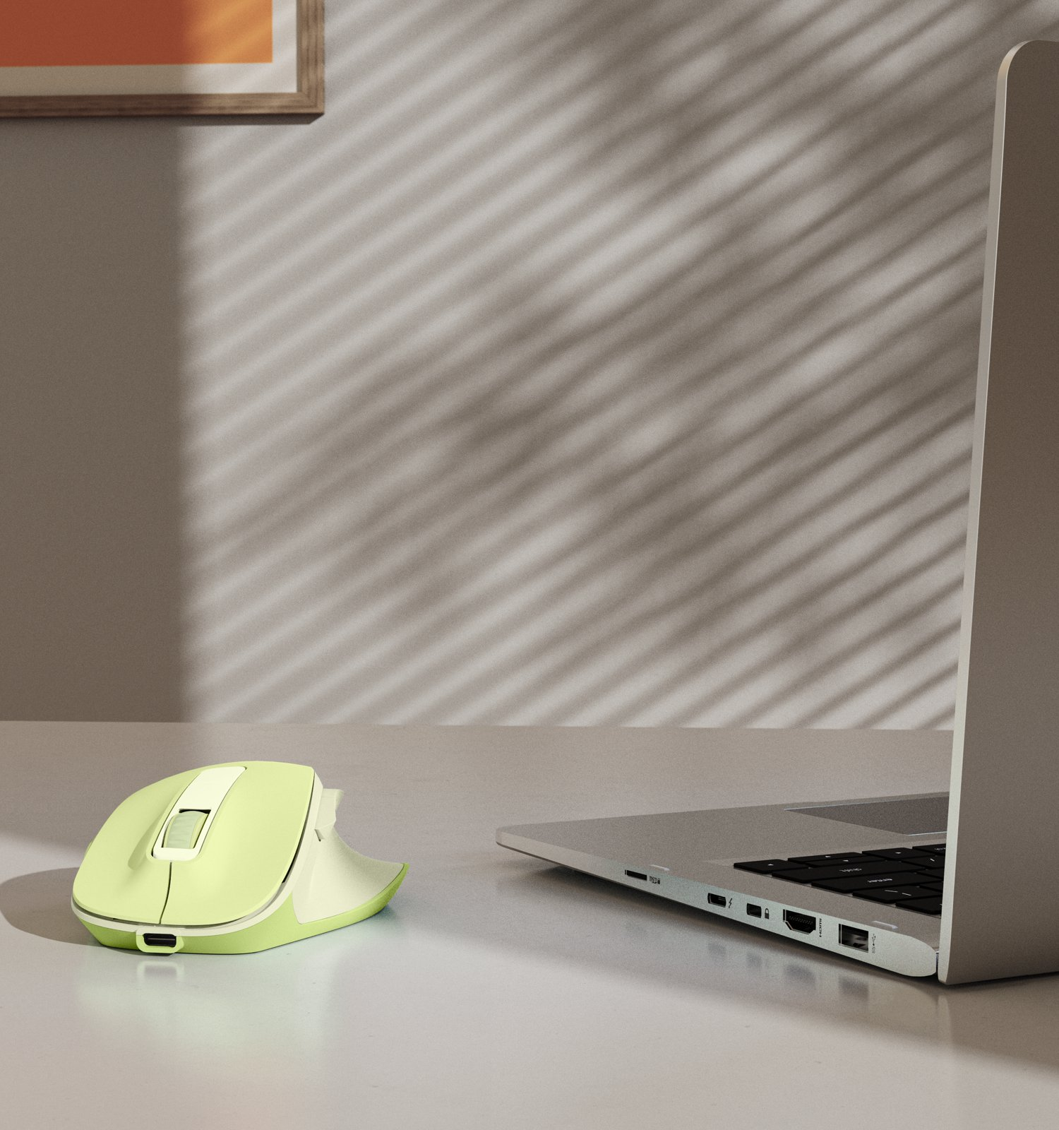 Un mouse wireless verde chiaro e un laptop su un tavolo bianco con ombre di finestre sulla parete.