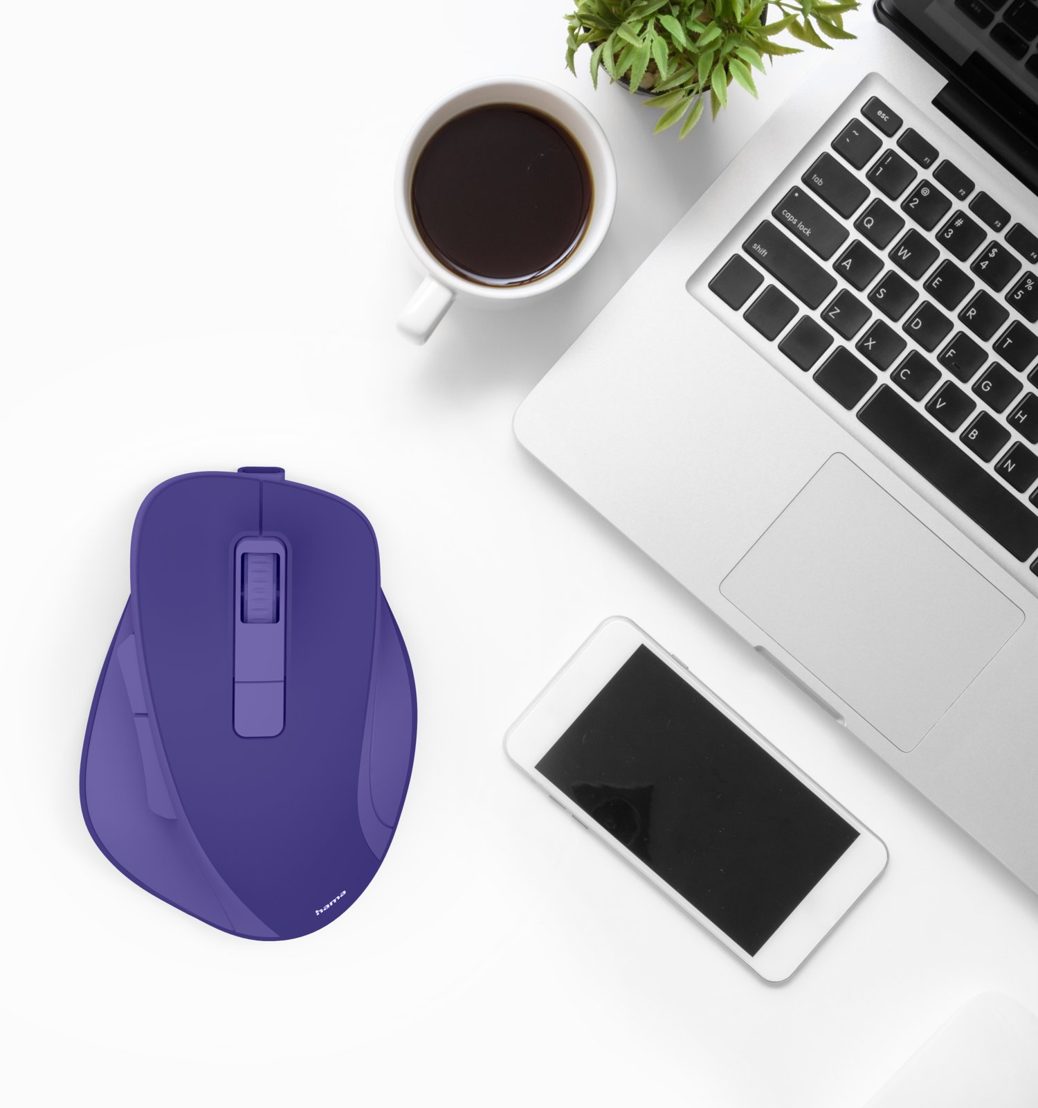 Lila Computermaus auf weißem Schreibtisch mit Laptop, Kaffeetasse, Smartphone und Pflanze.