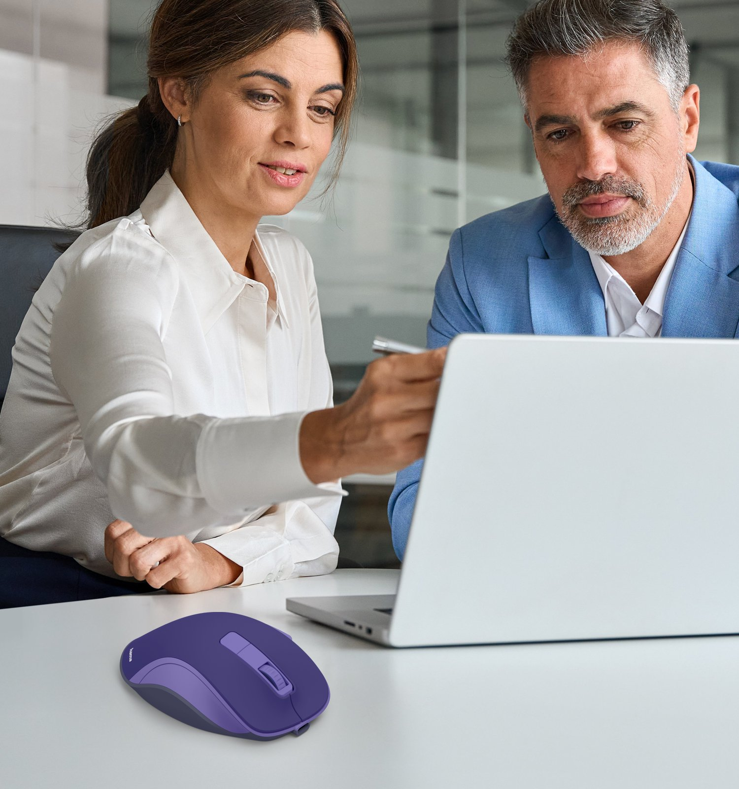 Eine Frau in Weiß und ein Mann in Blau sitzen vor einem Laptop; davor liegt eine violette Computermaus.