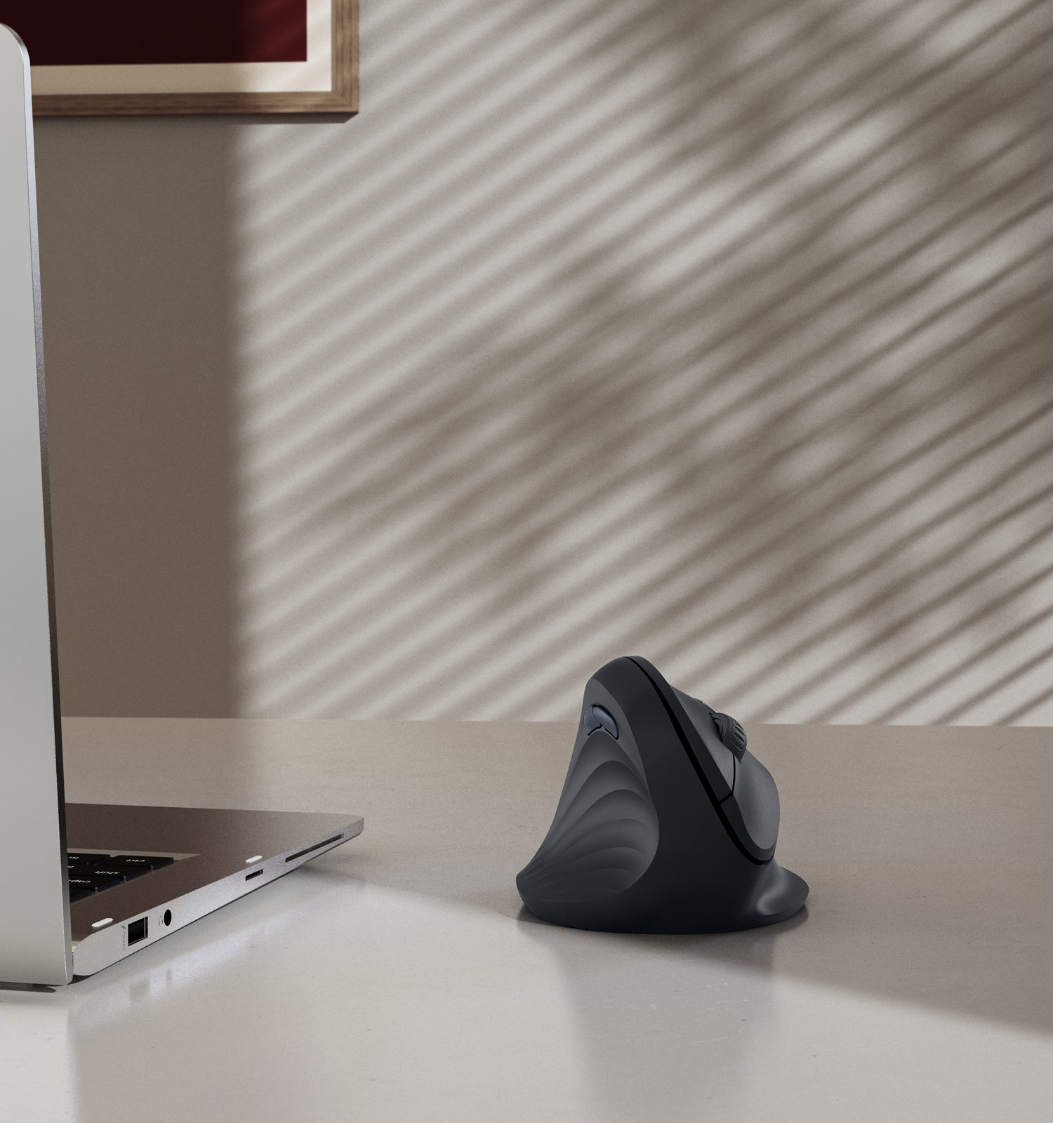 Un ratón vertical ergonómico negro en un escritorio junto a un portátil.