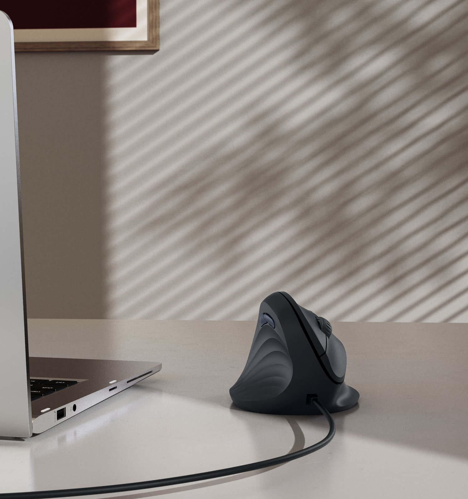 Un ratón vertical ergonómico negro descansa sobre un escritorio junto a un portátil.