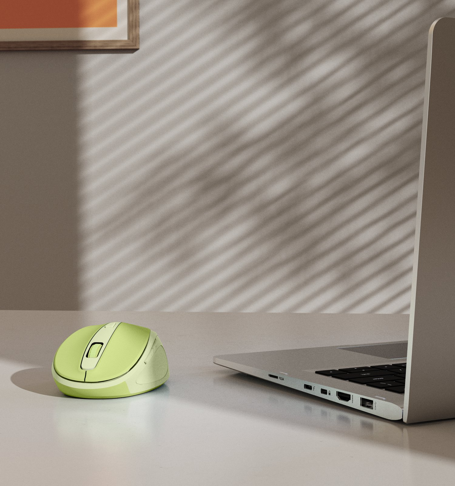 Un mouse wireless verde chiaro e un laptop sono su una scrivania bianca contro una parete con ombre.