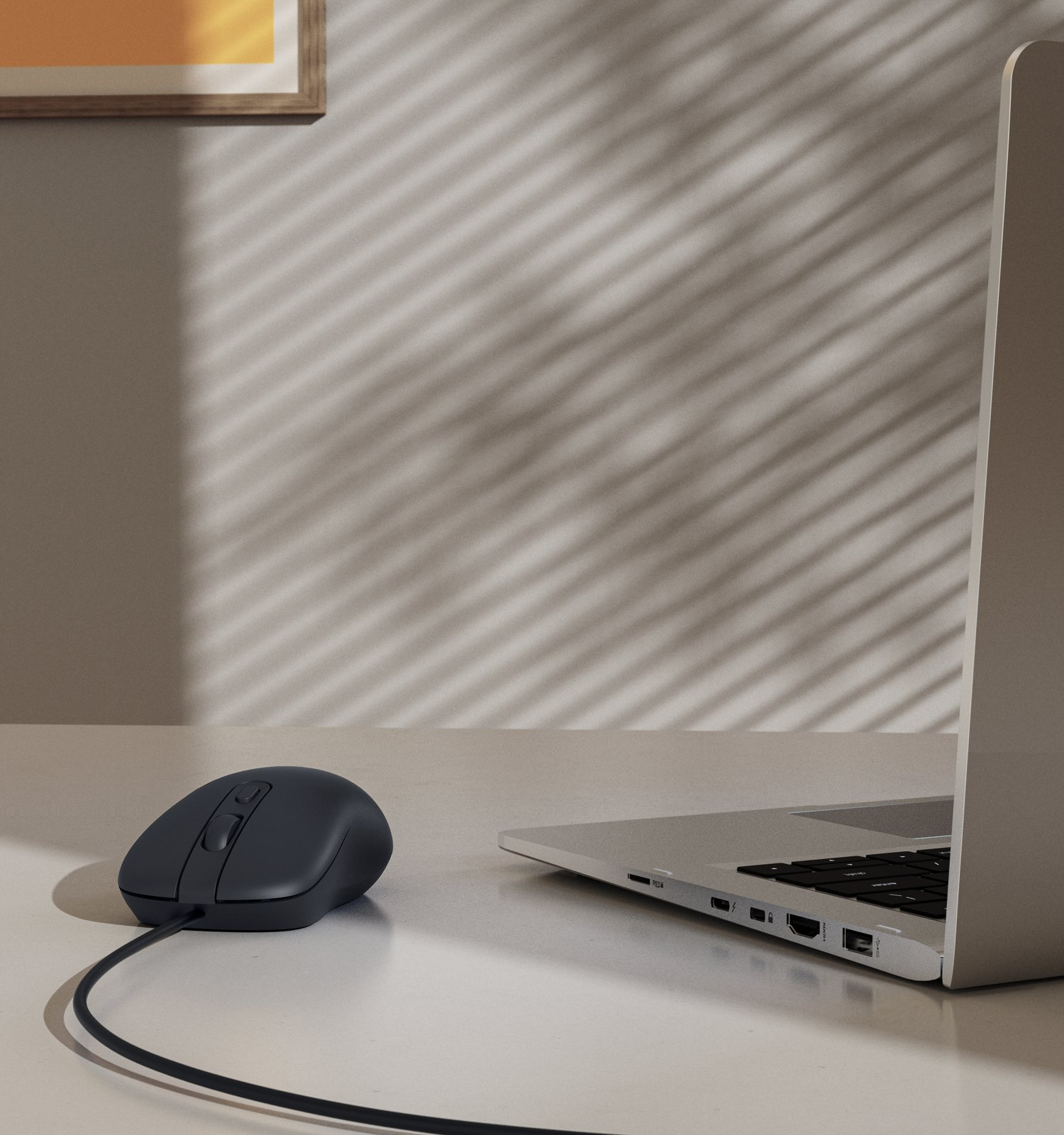 Un ratón con cable gris y un portátil sobre una mesa blanca frente a una pared con sombras de persiana.