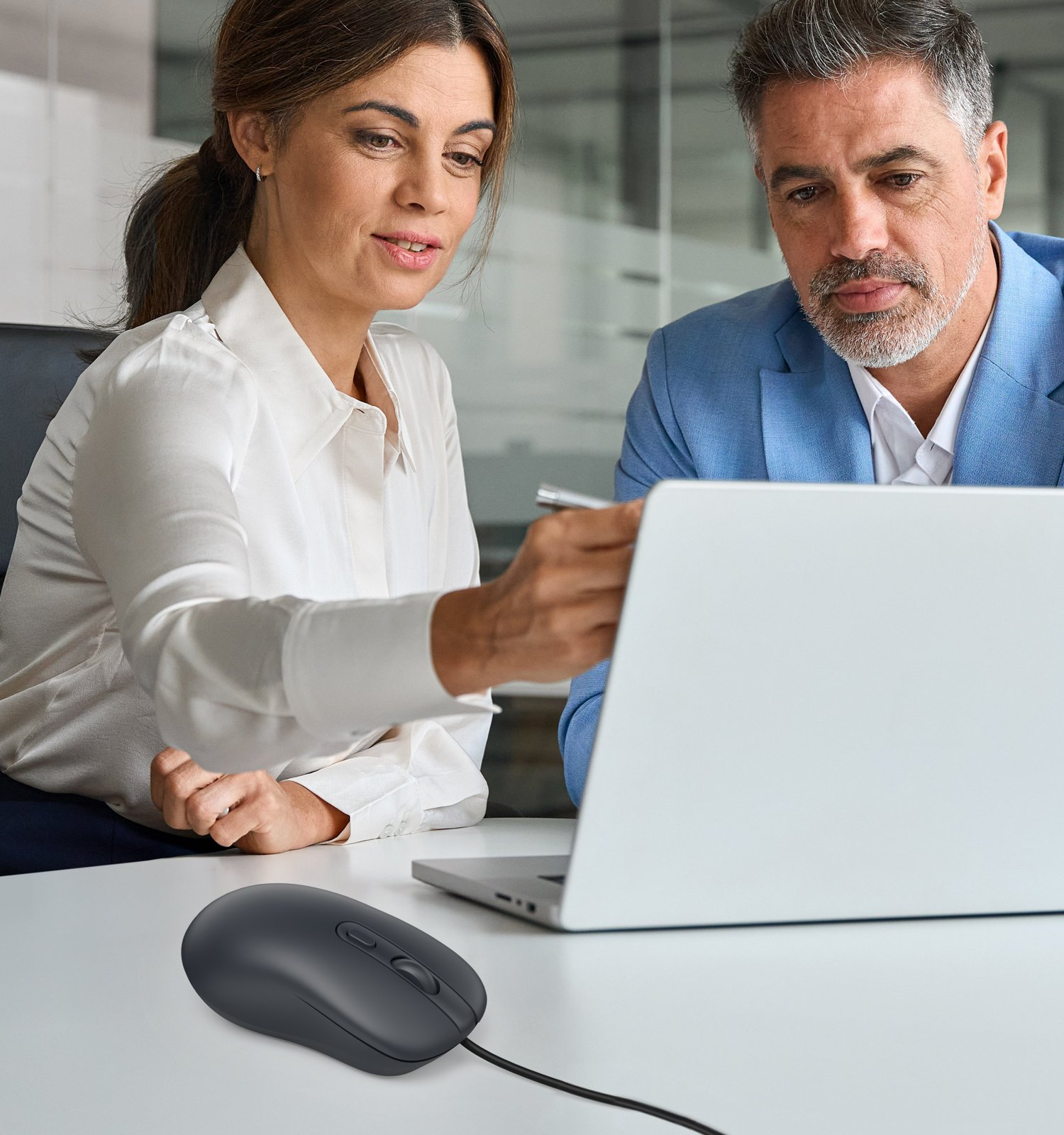 Una mujer de blanco y un hombre de azul miran una laptop juntos en una mesa.