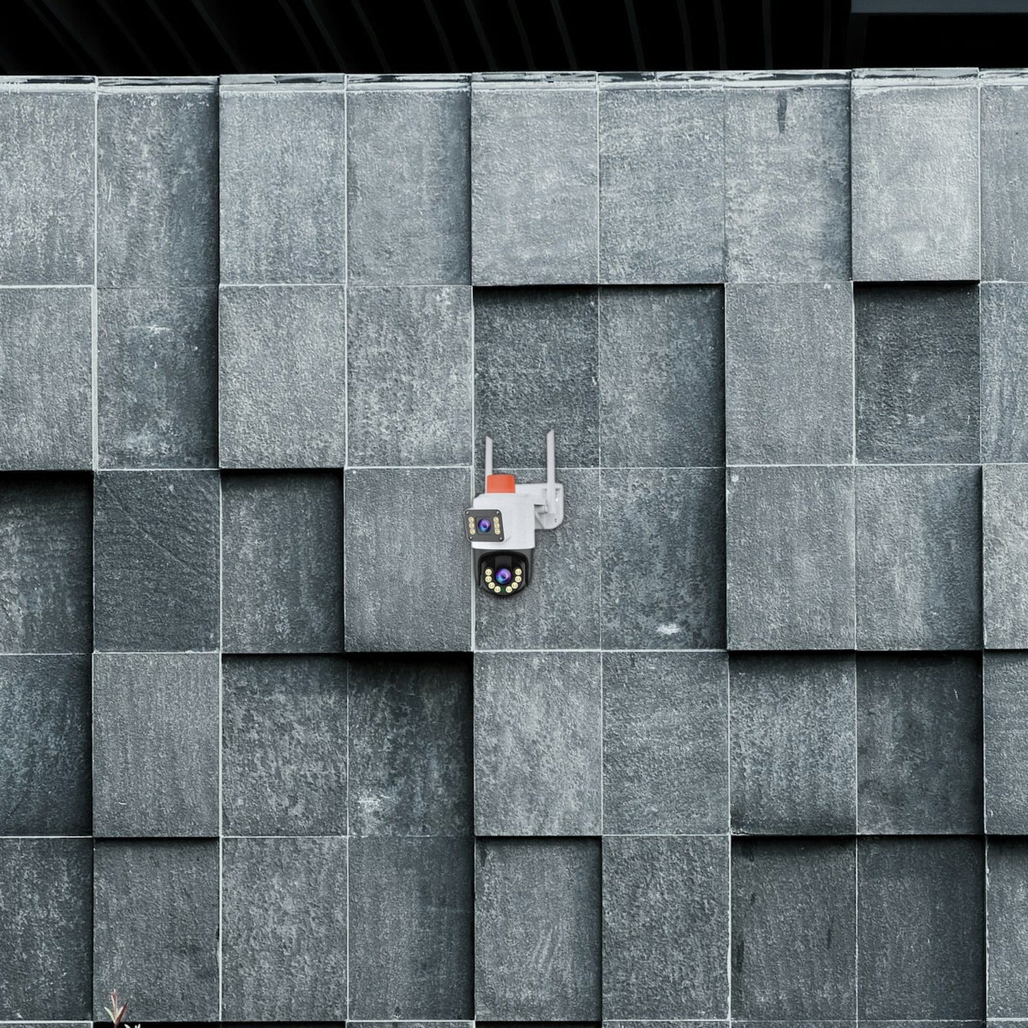 Una cámara de seguridad blanca con antenas está montada en una pared de piedra gris texturizada.