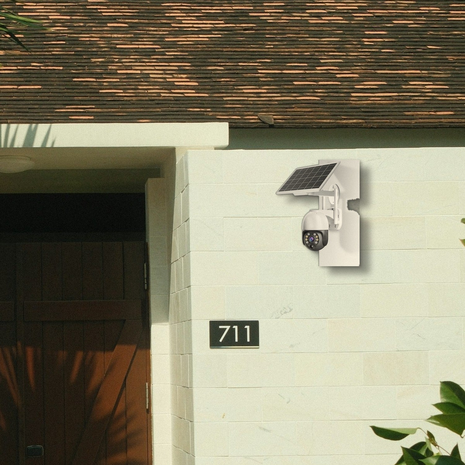 Una cámara de seguridad con panel solar en una pared de ladrillo blanco junto a una puerta de madera con el número 711.