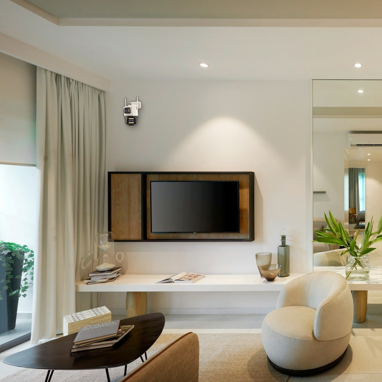 Salón moderno con televisor de pared, cámara de seguridad, sillón blanco, mesa de centro y pared espejada.