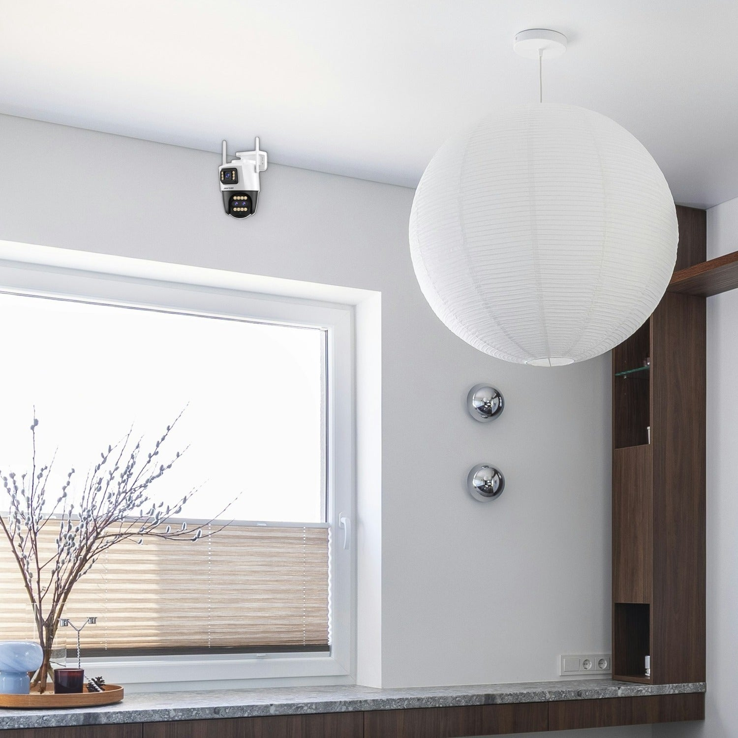 Sala con cámara de seguridad en la pared, lámpara redonda grande y ventana con estor plisado.
