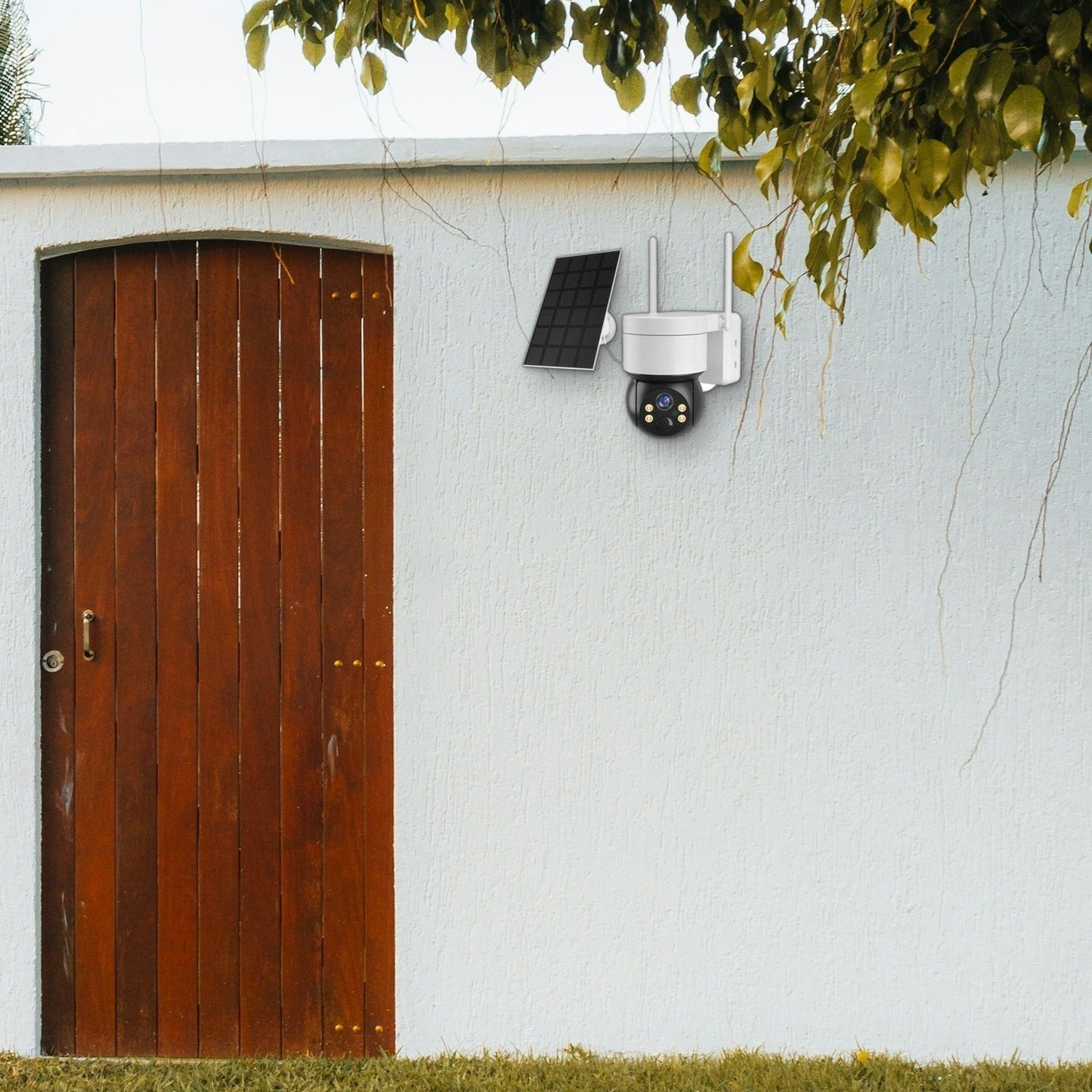 Una cámara de seguridad blanca con panel solar montada en una pared blanca junto a una puerta de madera.