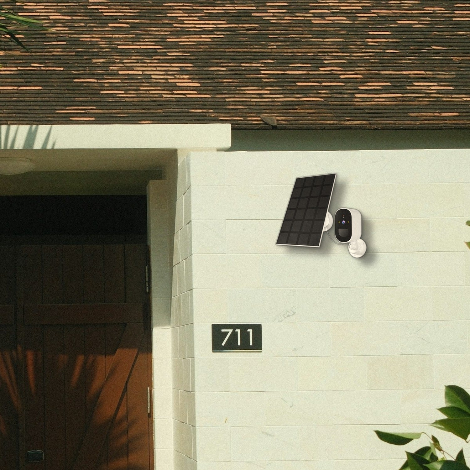 Una cámara de seguridad y panel solar en una pared blanca junto al n úmero 711 y una puerta de madera.
