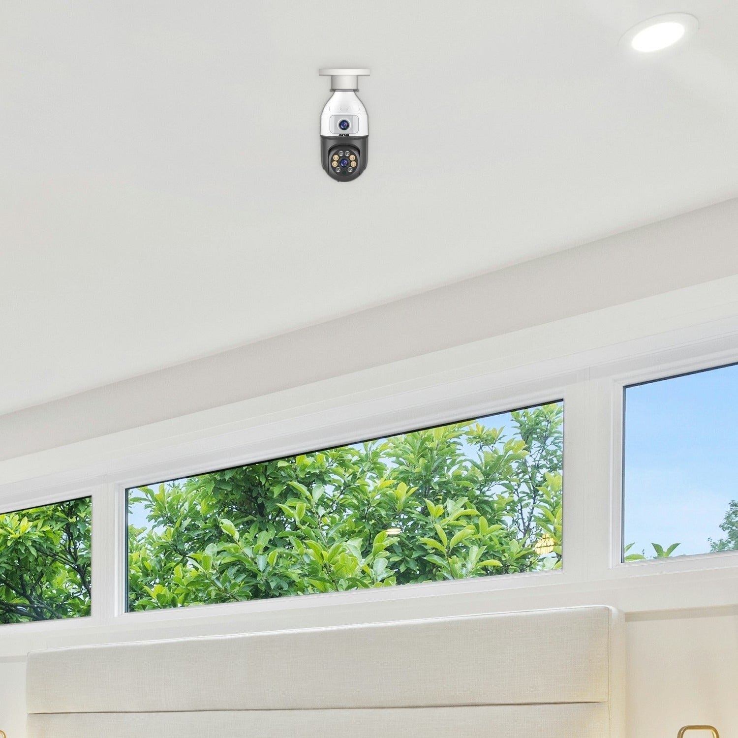 Una telecamera di sicurezza è montata su un soffitto bianco sopra finestre con vista sul verde.