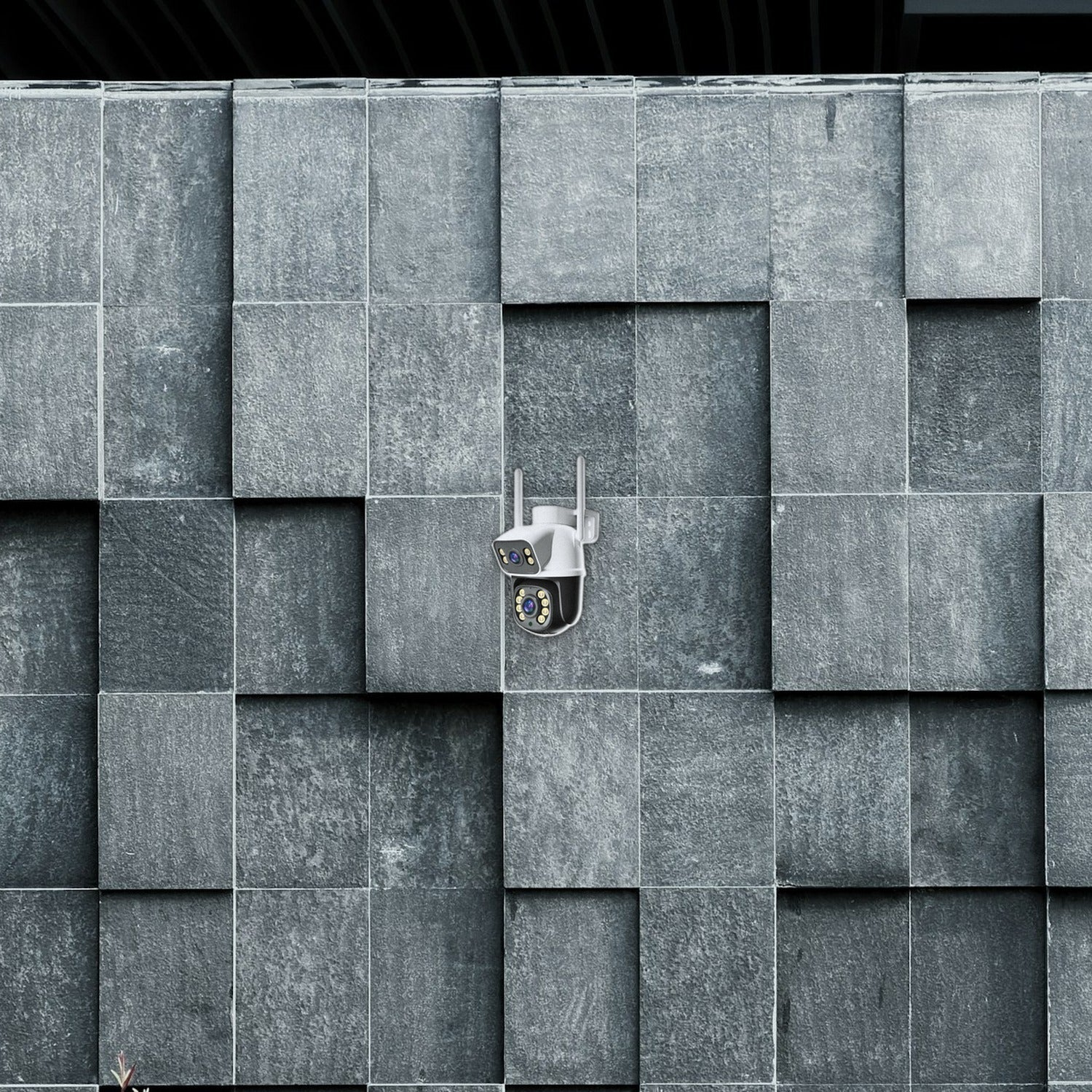 Una cámara de seguridad blanca con dos antenas montada en una pared de piedra gris texturizada.