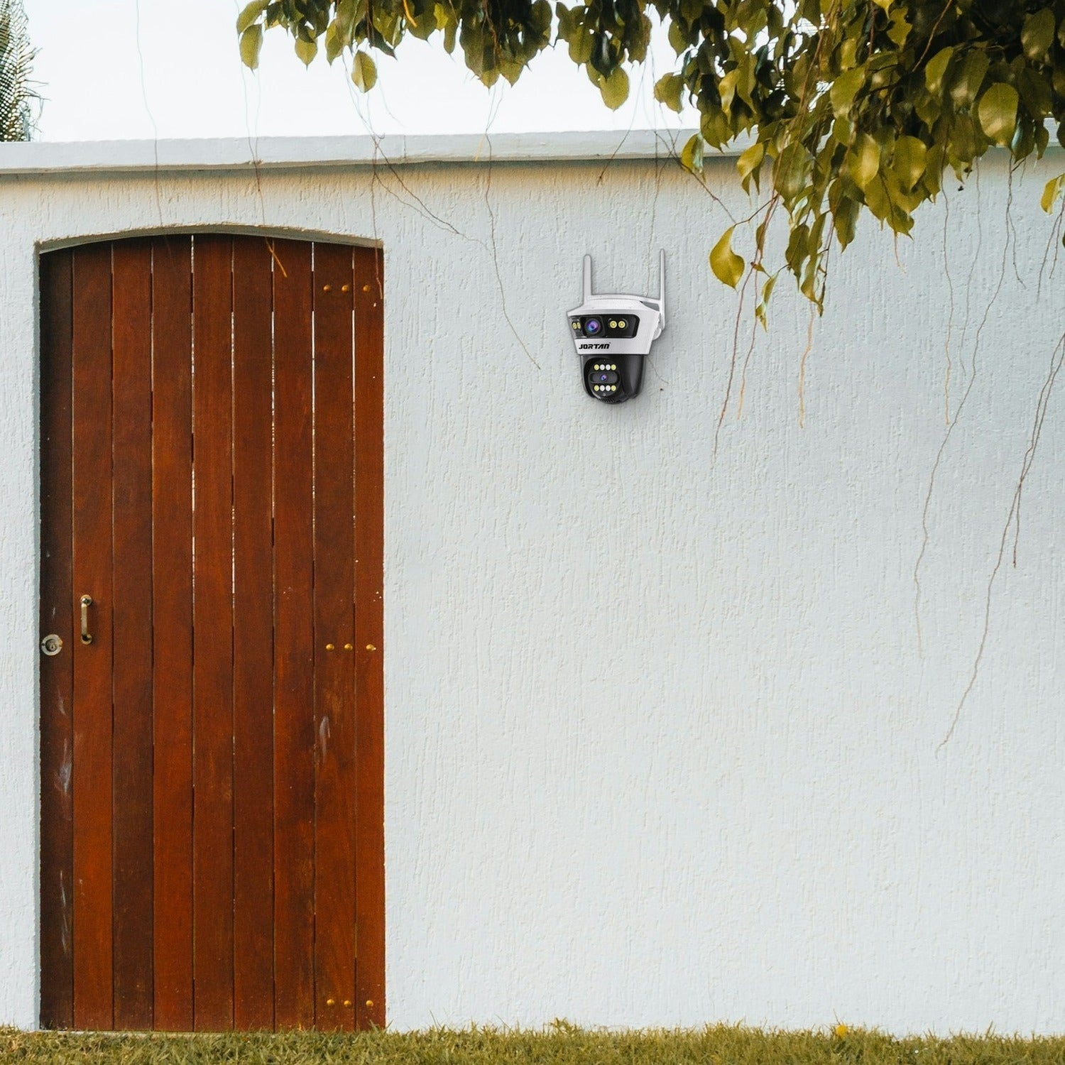 Una cámara de seguridad est á montada en una pared blanca junto a una puerta de madera.