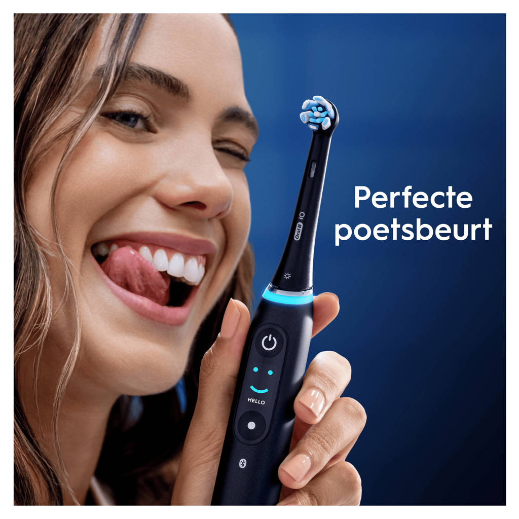 Eine Frau lächelt und leckt ihre Lippen, während sie eine schwarze Oral-B Zahnbürste vor blauem Hintergrund hält.